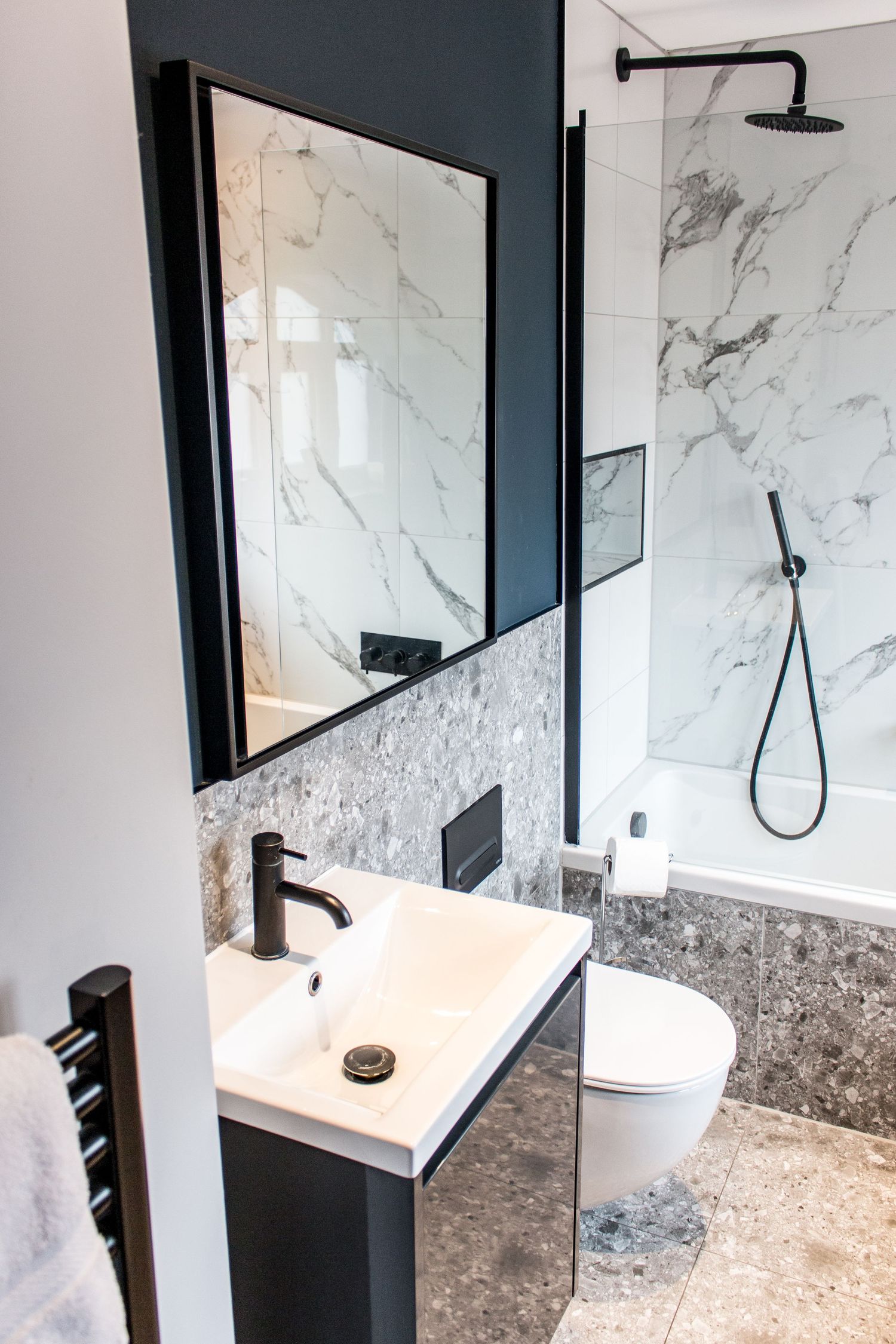 Contemporary bathroom featuring marble tiles, black fixtures, and glass shower enclosure.