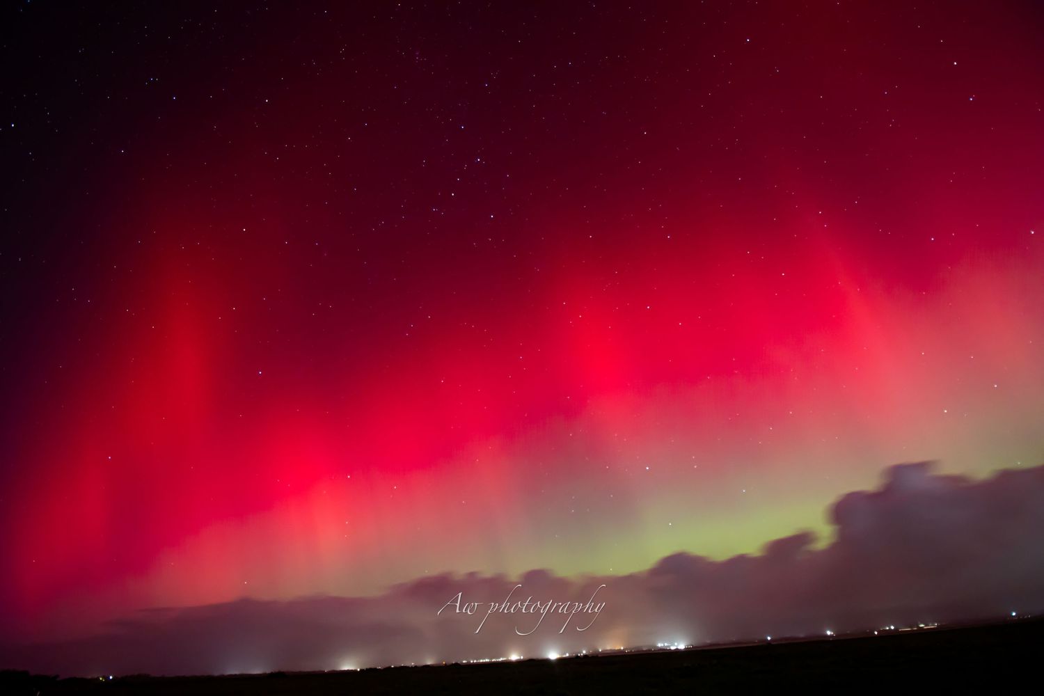 Spectacular red aurora borealis display illuminates the horizon with city lights below.