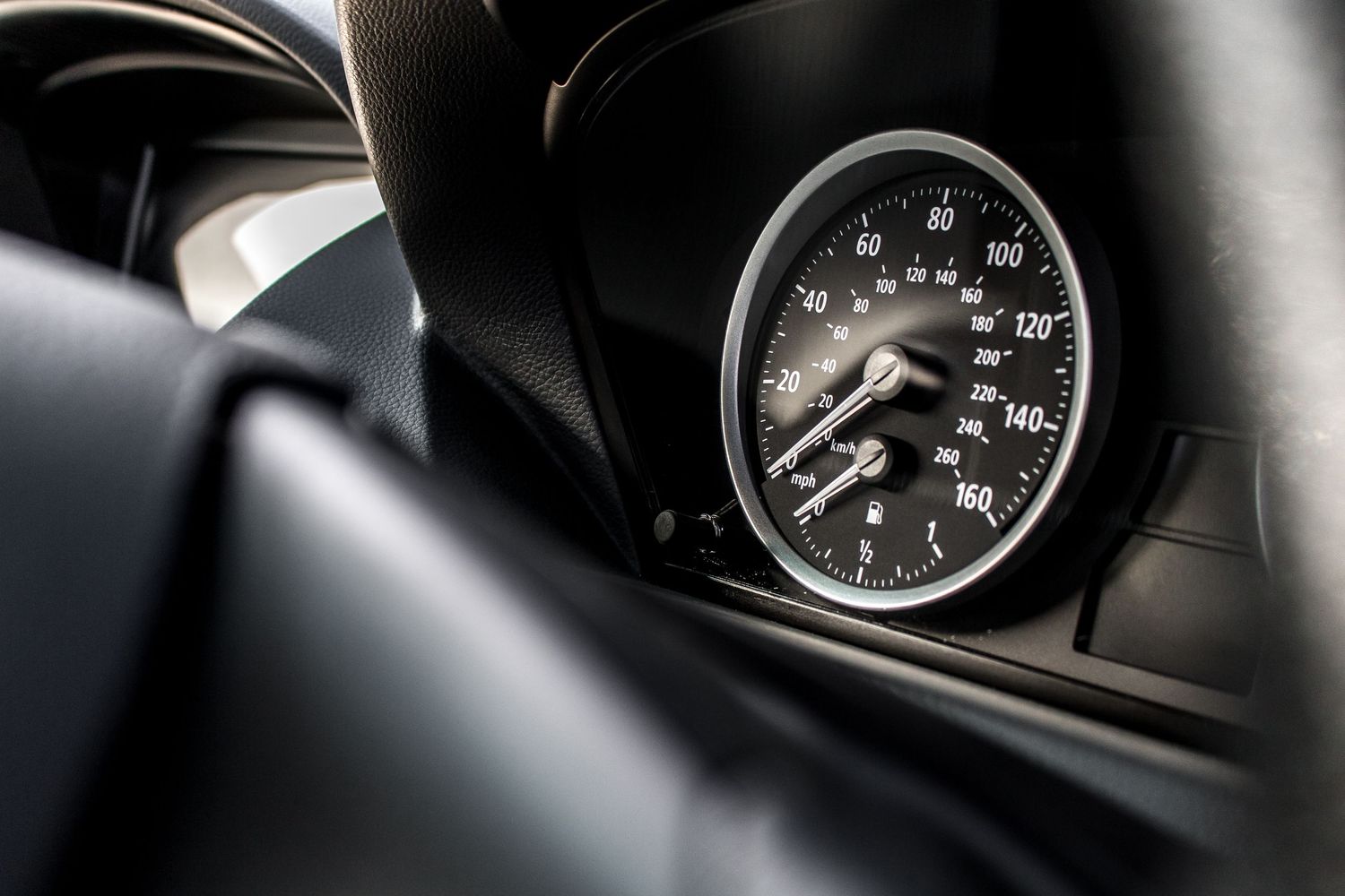 Close-up of a sleek black car speedometer showing 140 mph, set in a luxury vehicle dashboard interior.