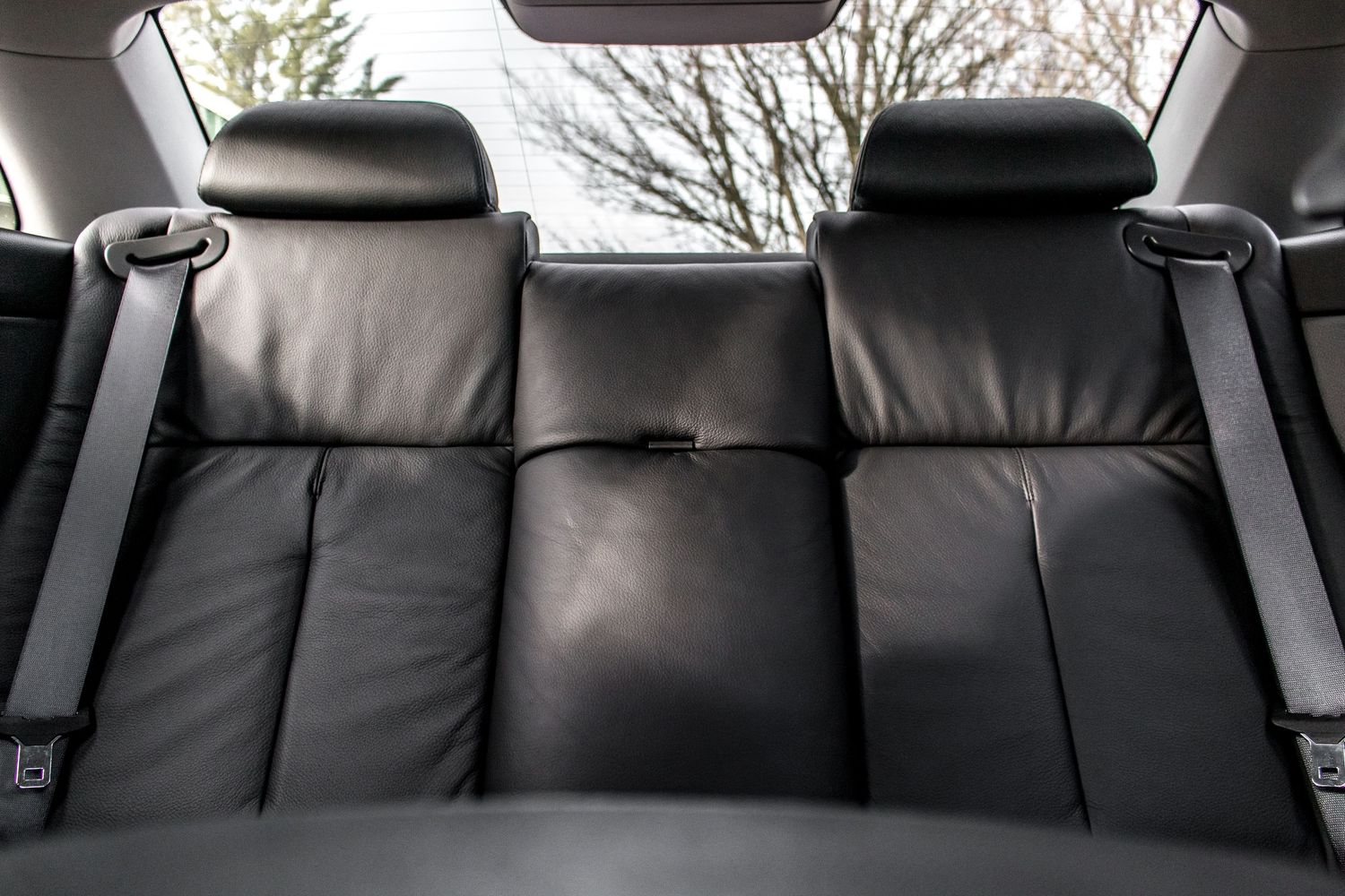 Black leather rear car seat with three headrests and seatbelts visible, viewed from inside a vehicle.
