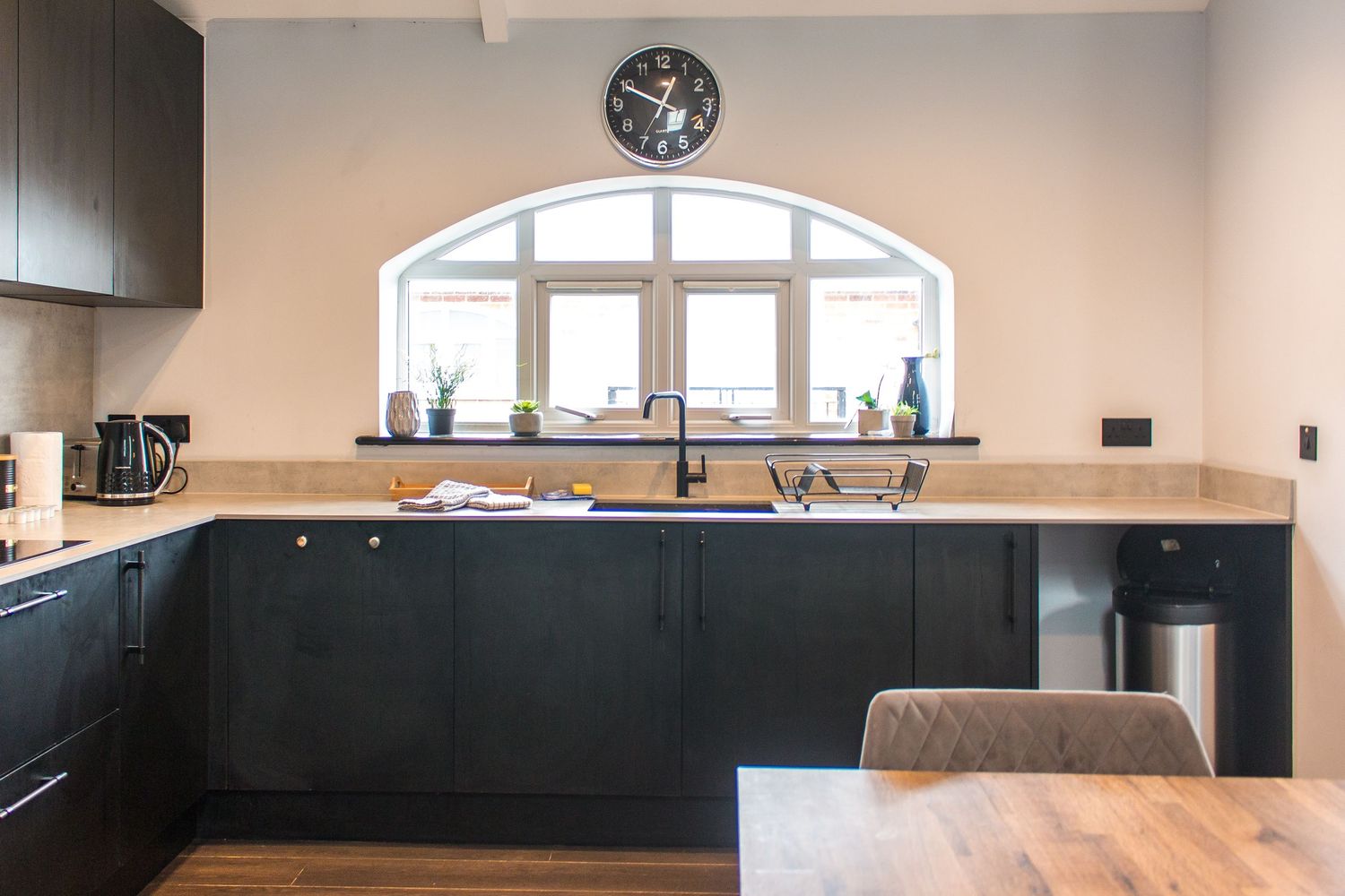 Sleek black kitchen cabinetry with arched window and modern appliances.