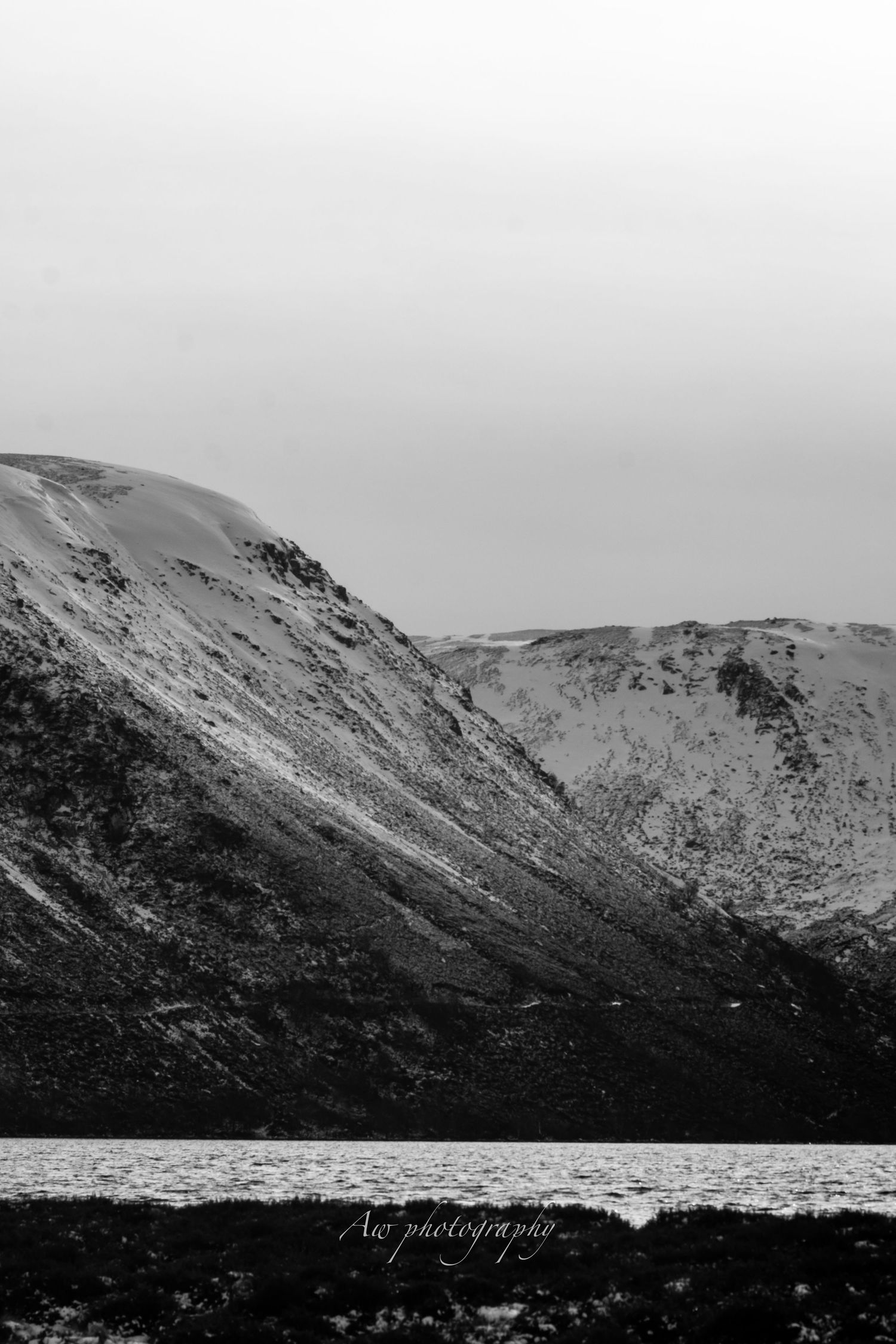 Snow-capped mountain peaks under a moody grey sky in a dramatic black and white landscape.