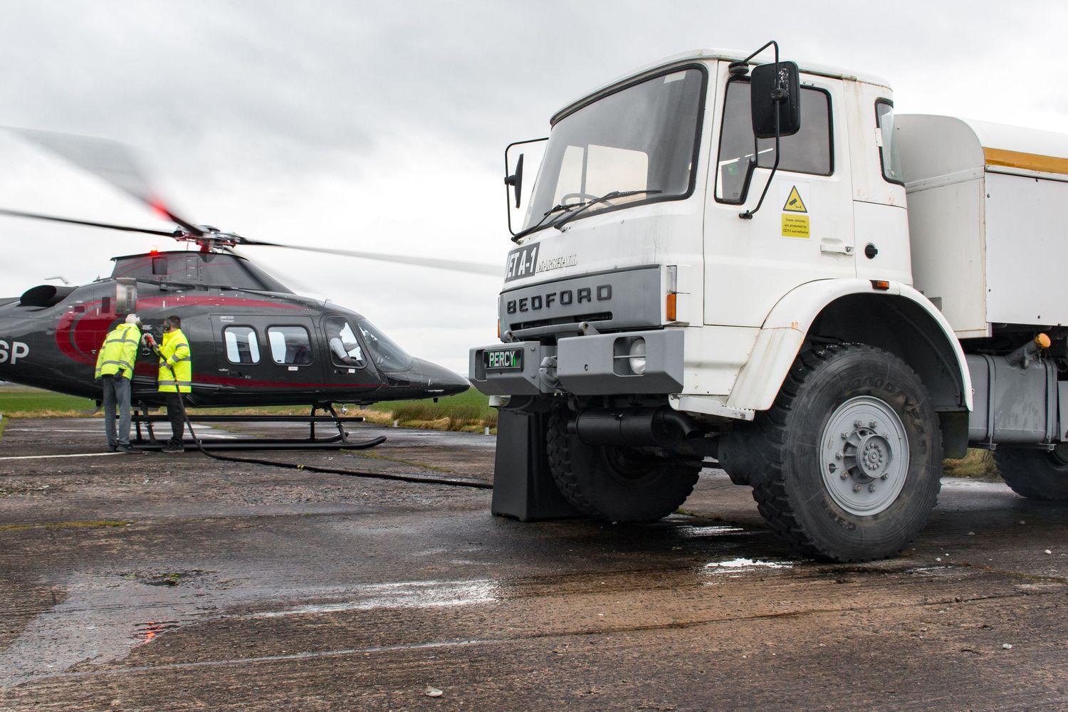 Service vehicles and equipment positioned near parked helicopters on wet tarmac.