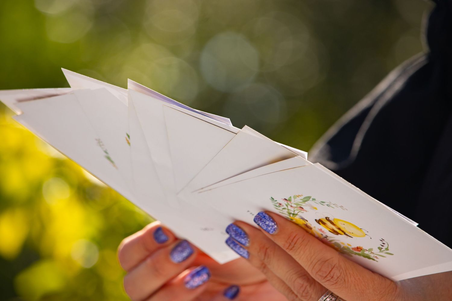 Close-up of hands holding white paper cards with blue painted nails.