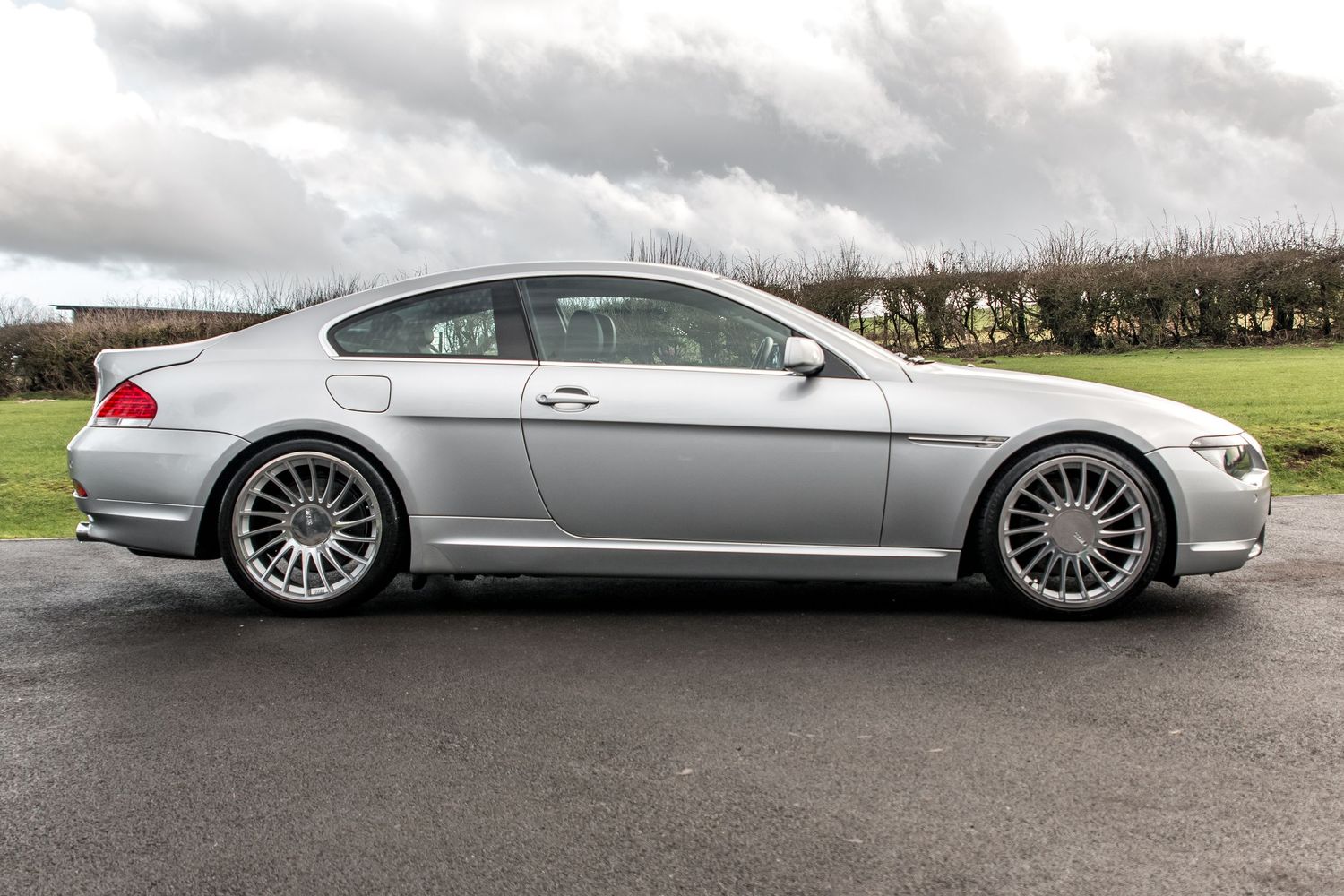 Silver BMW 6 Series coupe parked on tarmac, showcasing sleek profile with alloy wheels and fastback roofline.