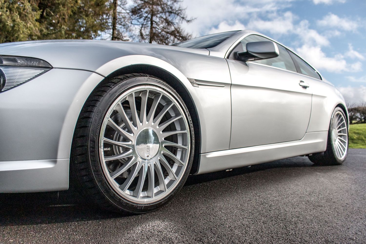 Silver BMW coupe with large multi-spoke alloy wheels on a paved surface, showcasing a low-profile stance.