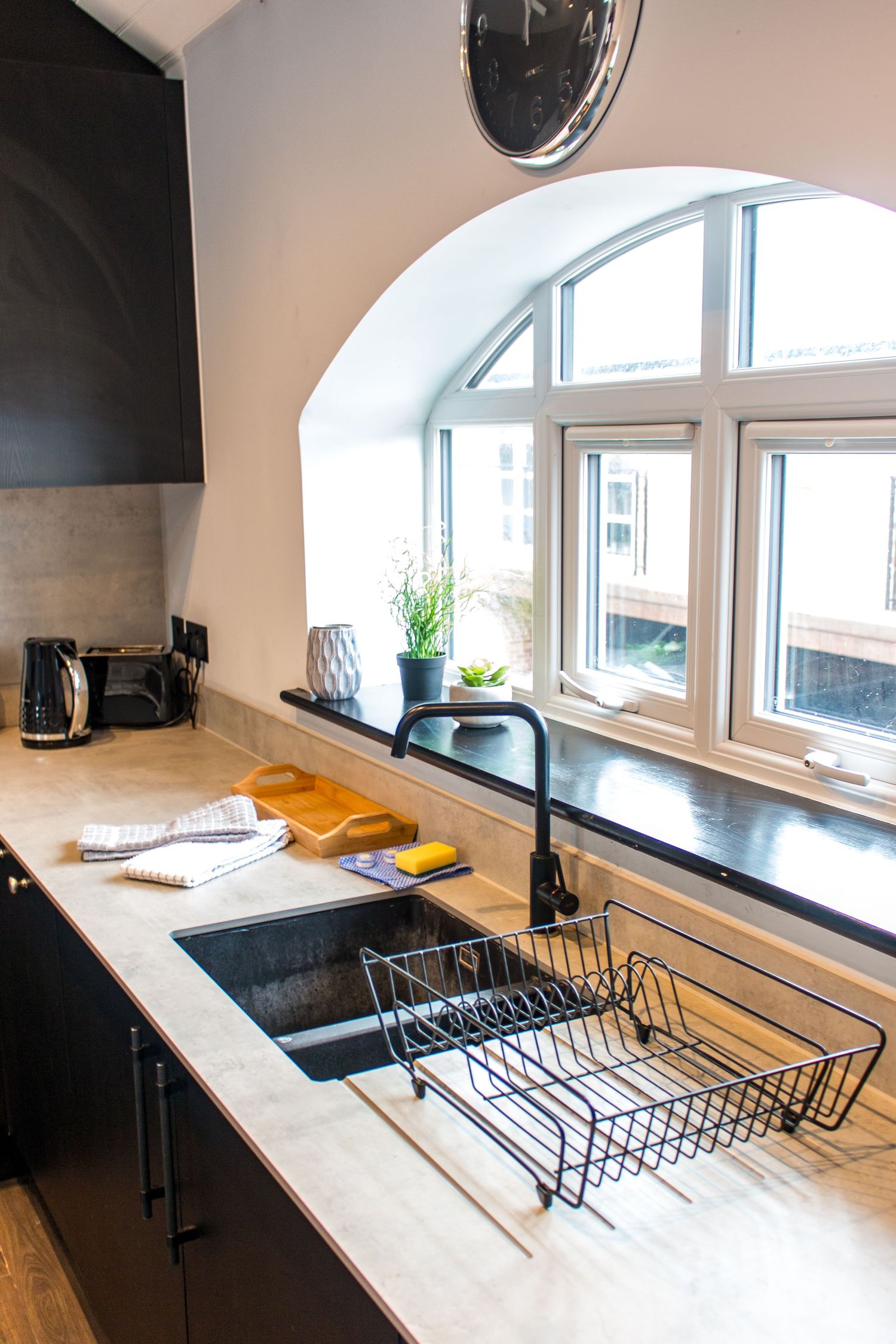 Minimalist kitchen counter with arched window and black dish drying rack against white surface.