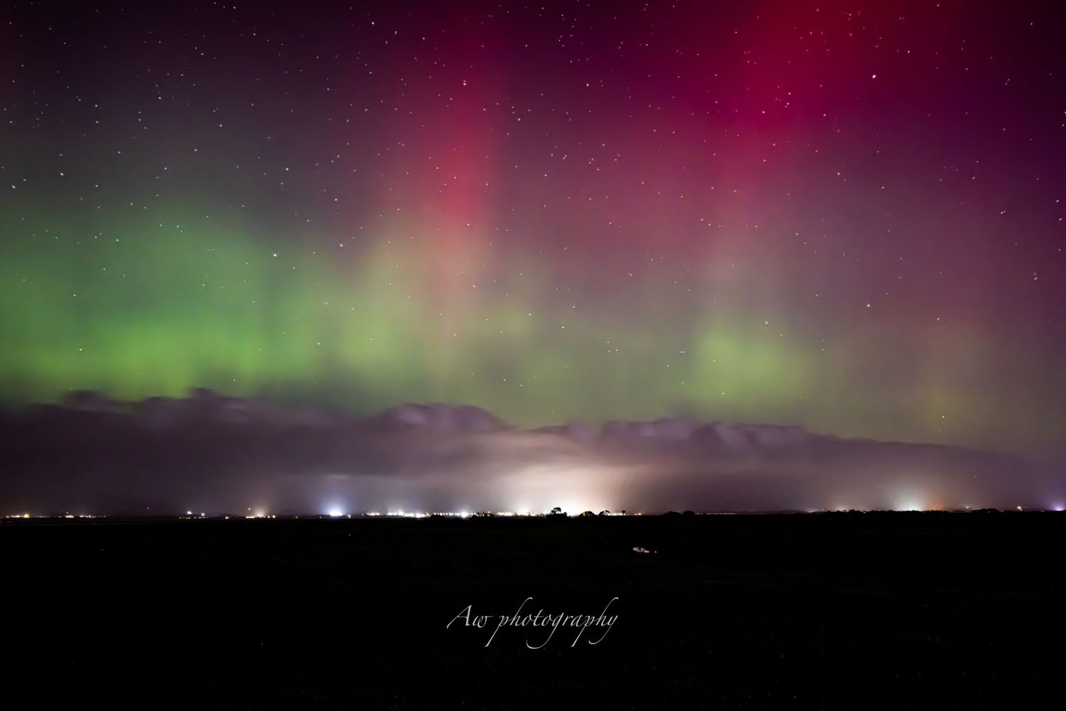 Vibrant red and green aurora borealis lights dance across the dark night sky.