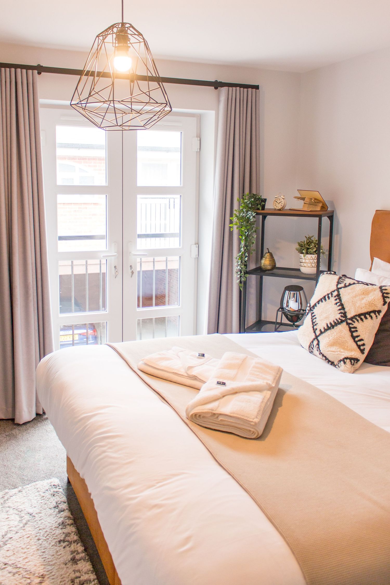 Modern bedroom with geometric pendant light, white bedding, and natural light streaming through windows.