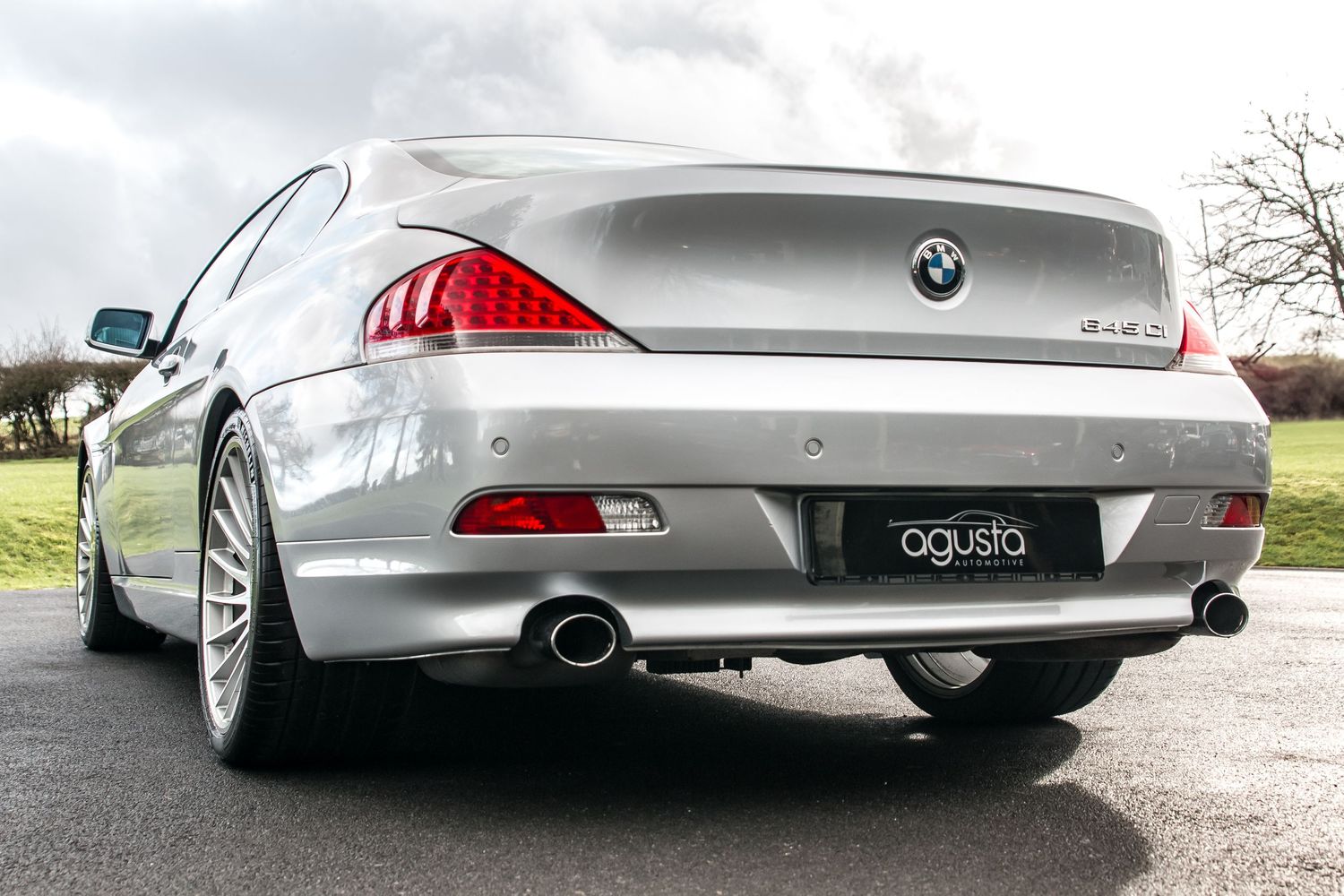 Silver BMW 6 Series coupe rear view with Agusta branding, dual exhaust tips, and alloy wheels on a paved surface.