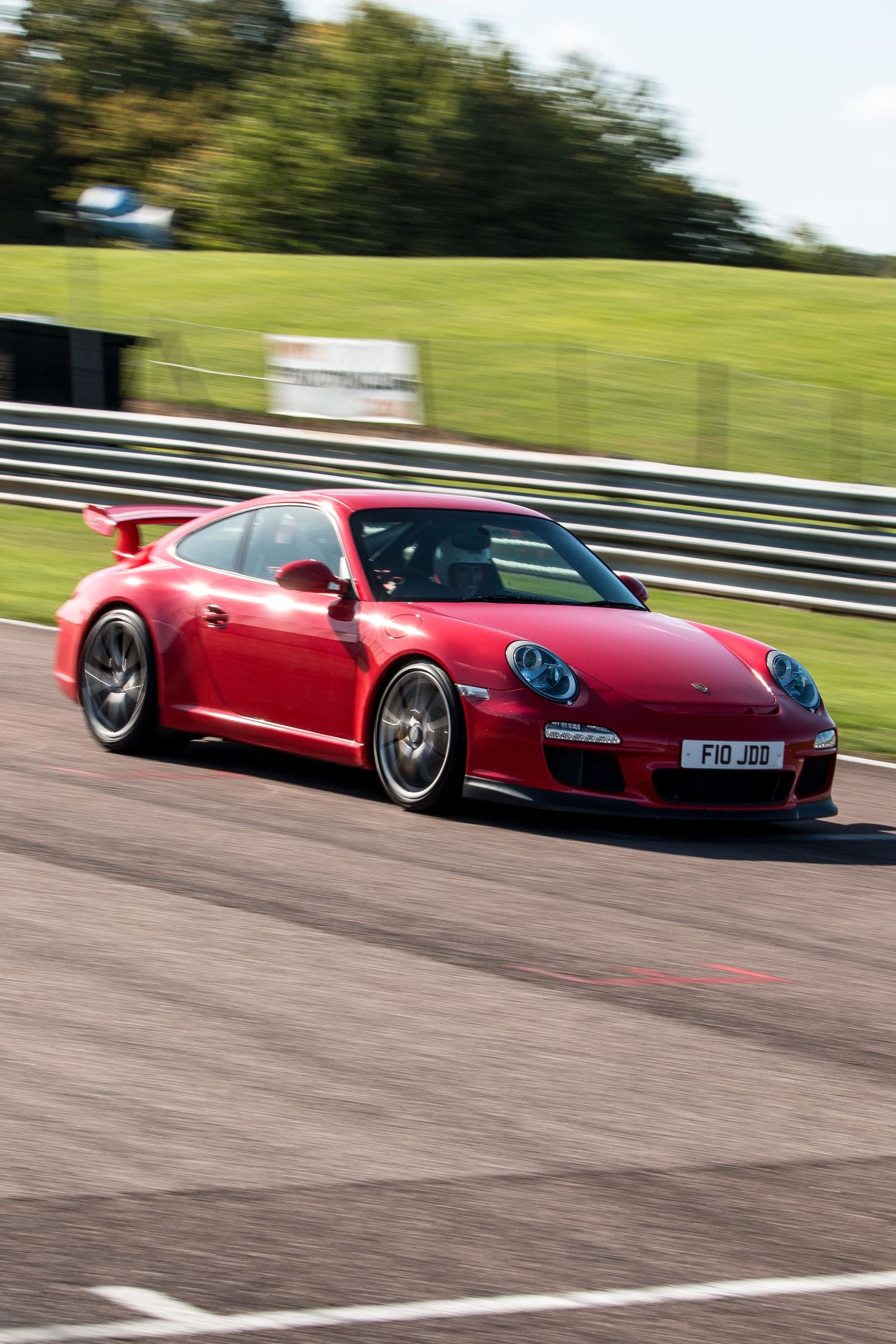 Red Porsche 911 GT3 racing on a track circuit, captured in motion with green grass and barriers in the background.