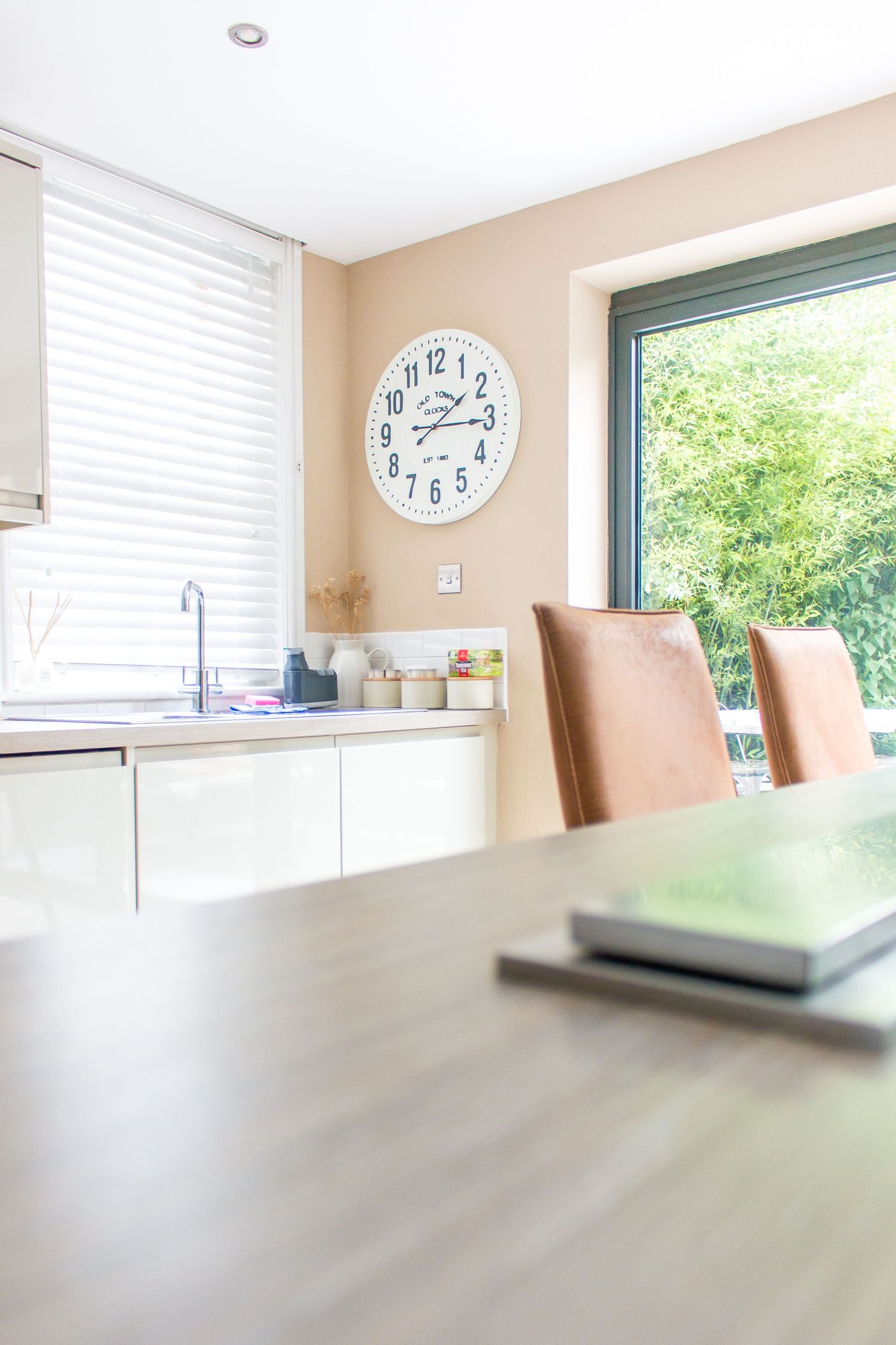 Modern white kitchen interior with natural light streaming through windows and a wall clock.