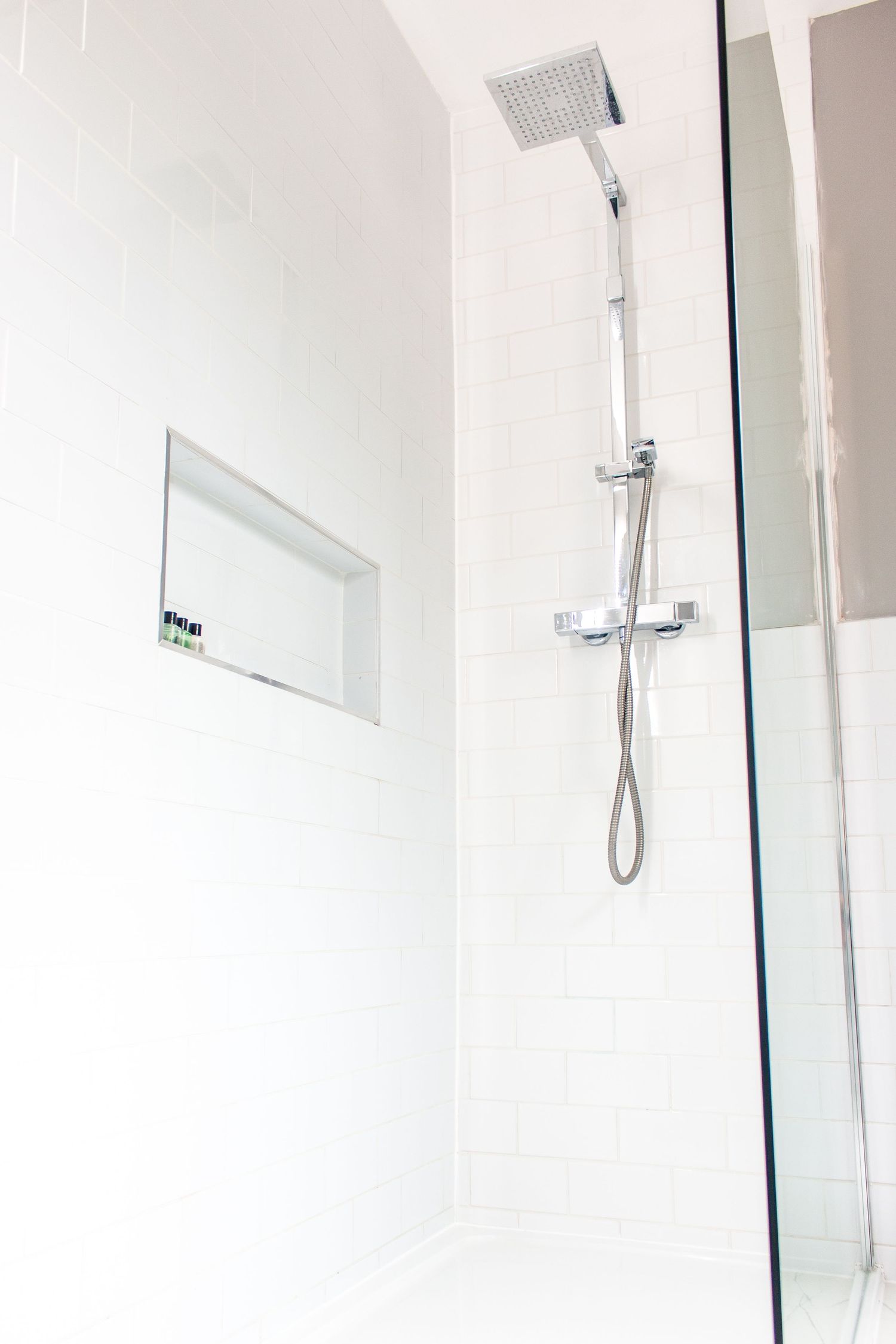 Modern glass shower enclosure with chrome rainfall showerhead and sleek white tiles.