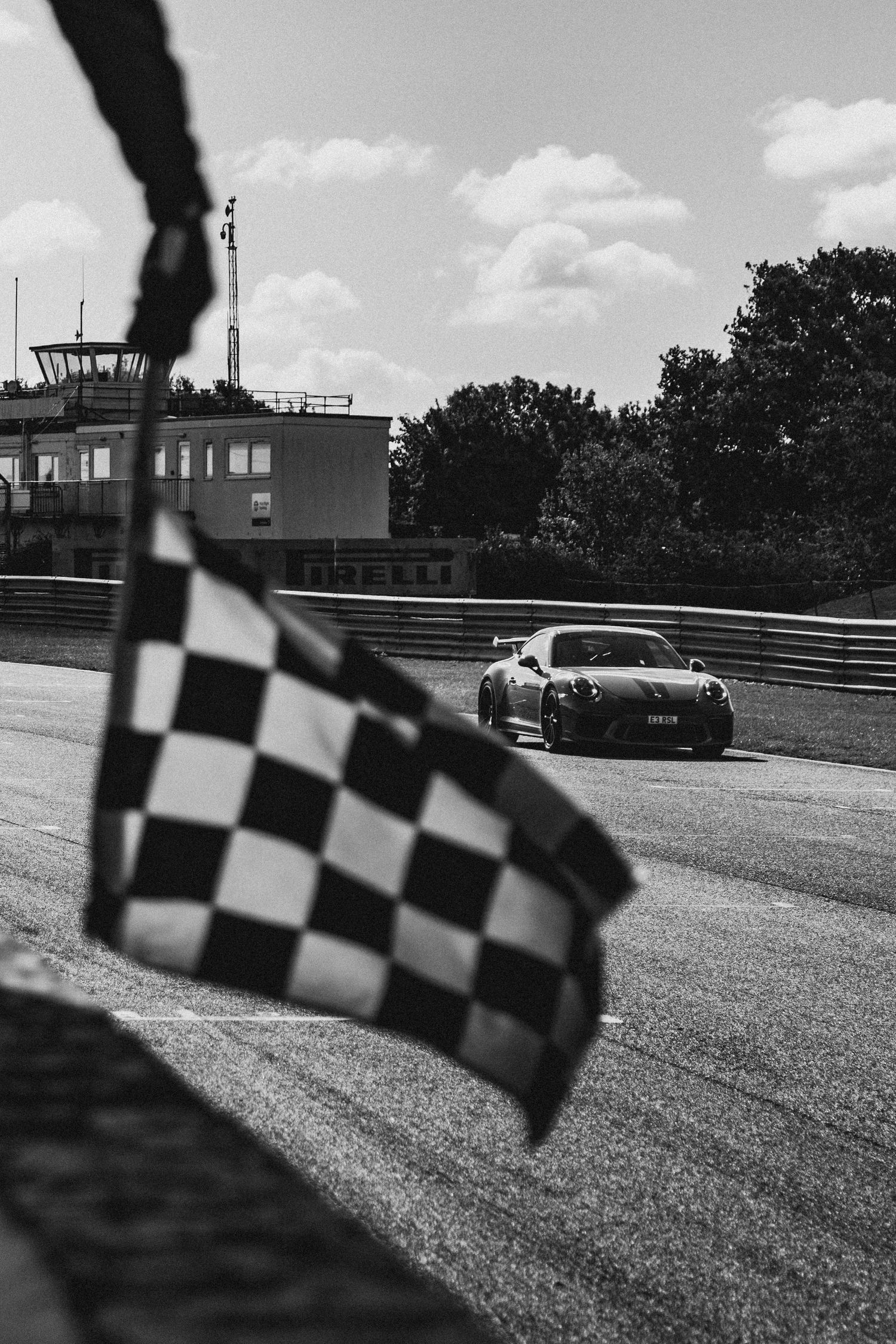 Race car on track with checkered flag in foreground, black and white photography.
