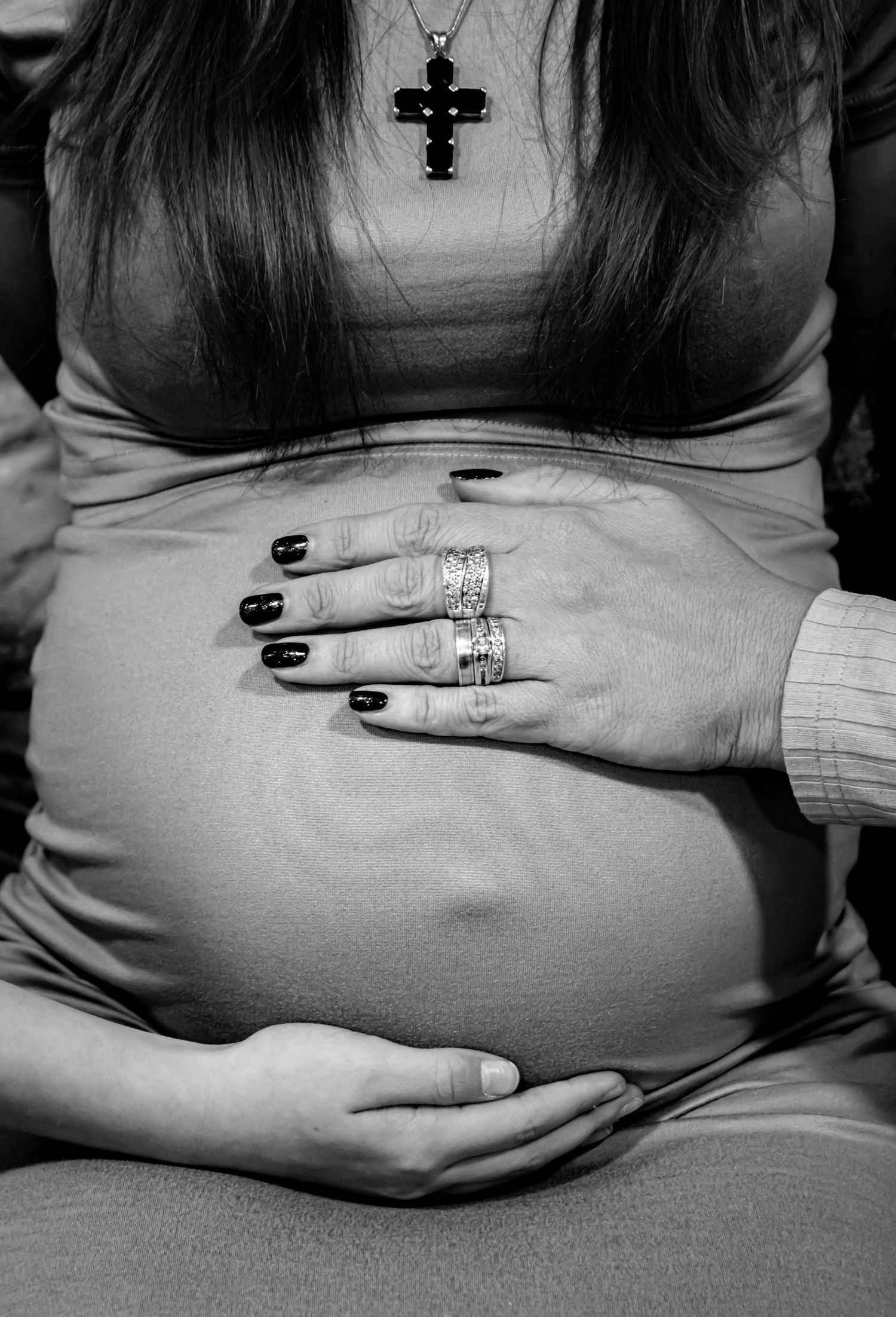 Close-up black and white photos of hands resting on a pregnant belly wearing rings.