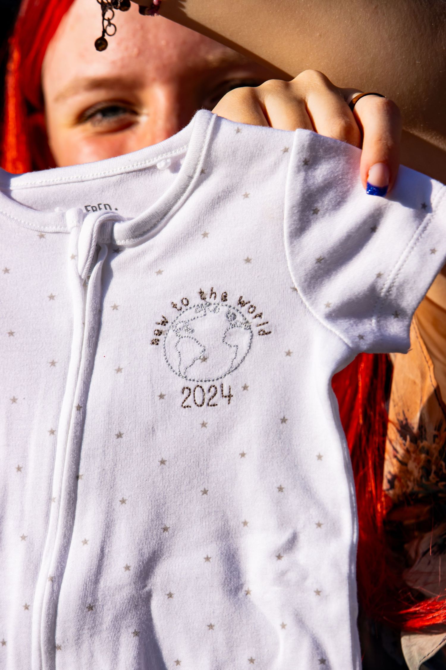 White infant bodysuit with delicate star patterns and '2024' text design.