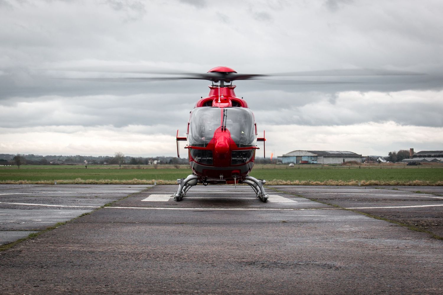 Red medical helicopter on runway under cloudy sky.