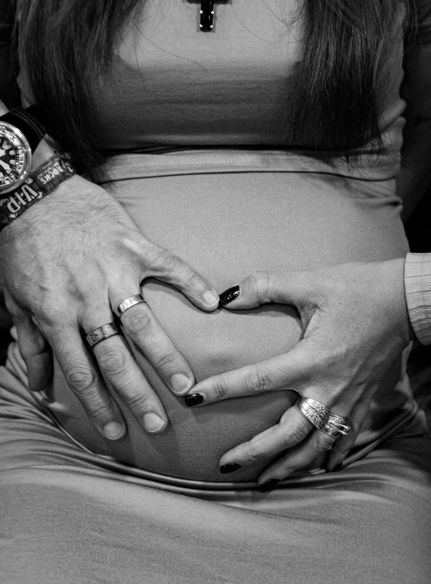 Black and white photo of hands forming a heart shape on a pregnant belly.