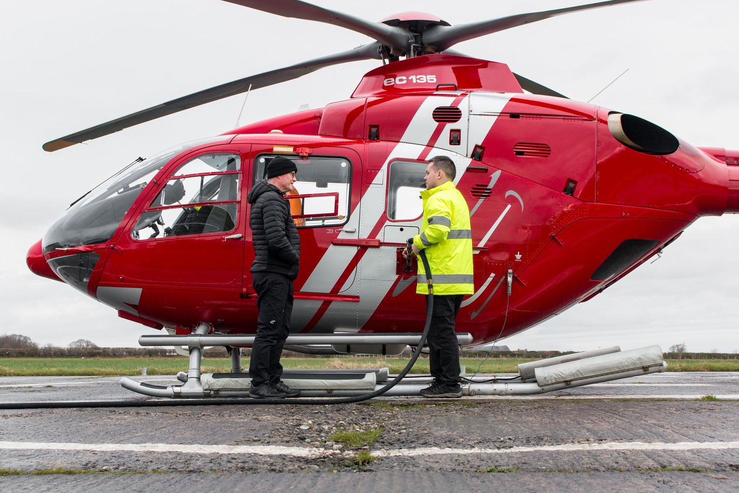 Red emergency helicopter with crew members on helipad.