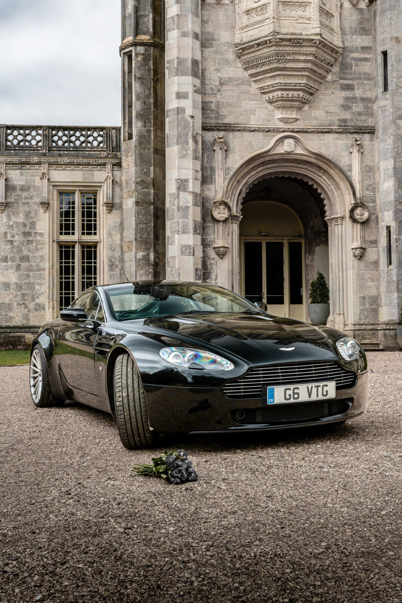 Black Aston Martin sports car parked in front of a grand stone castle.