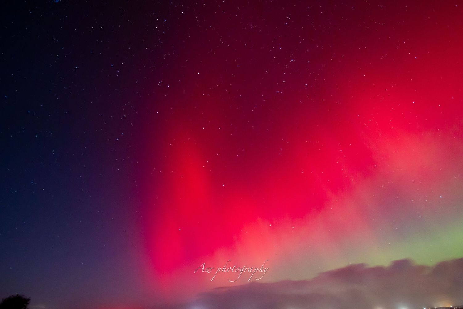 Intense red northern lights glow against the dark night sky with hints of green.