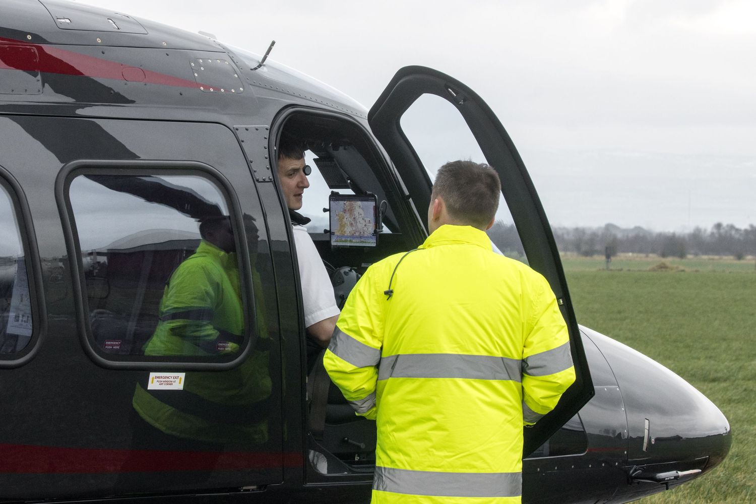 Ground crew in high-visibility gear inspecting black helicopter on tarmac.