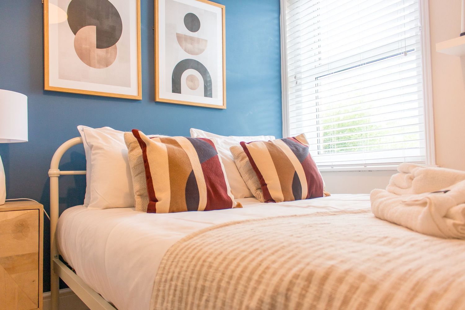 Minimalist bedroom with blue accent wall and geometric artwork above white bedding.
