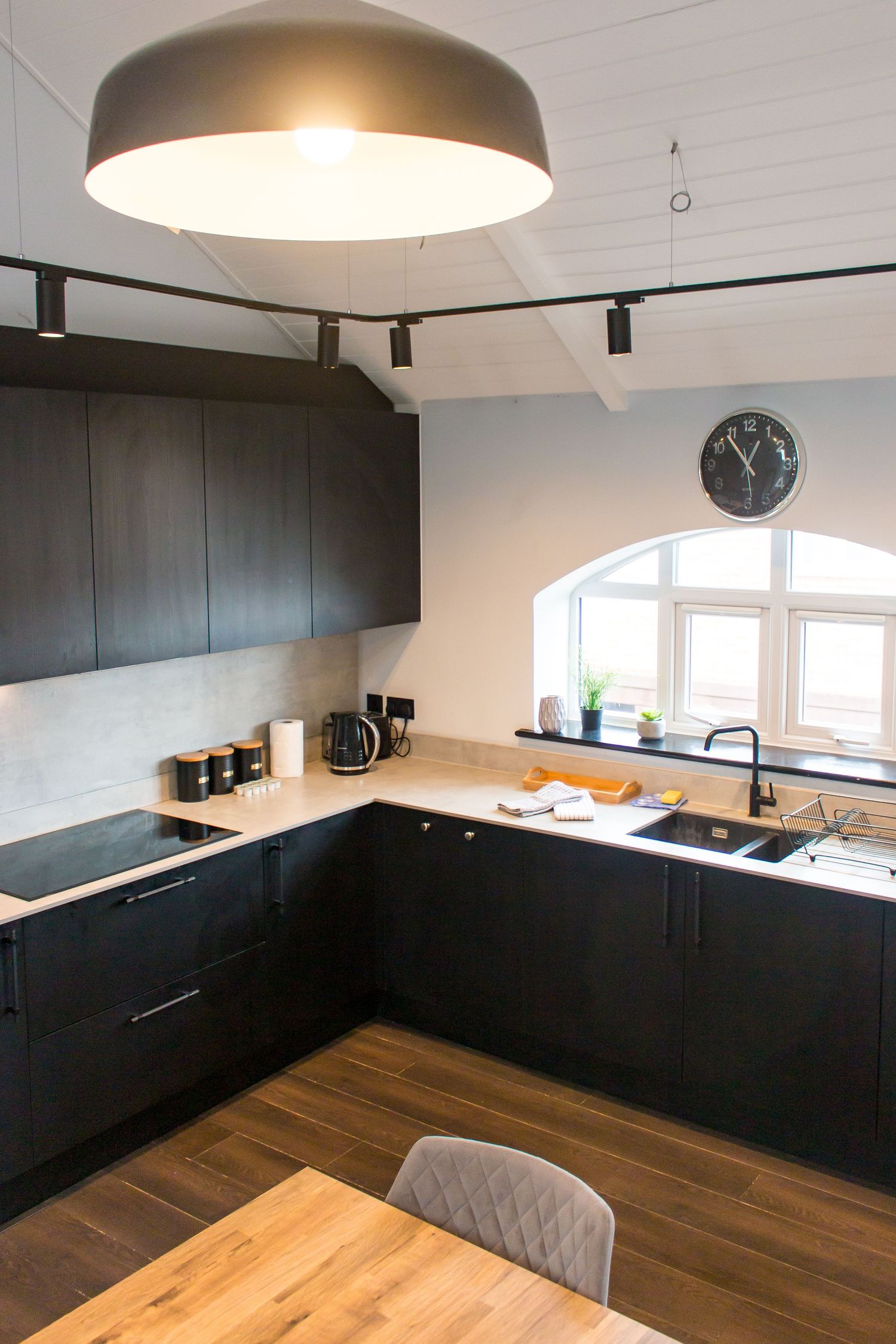 Contemporary black kitchen with wooden floors and pendant lighting.