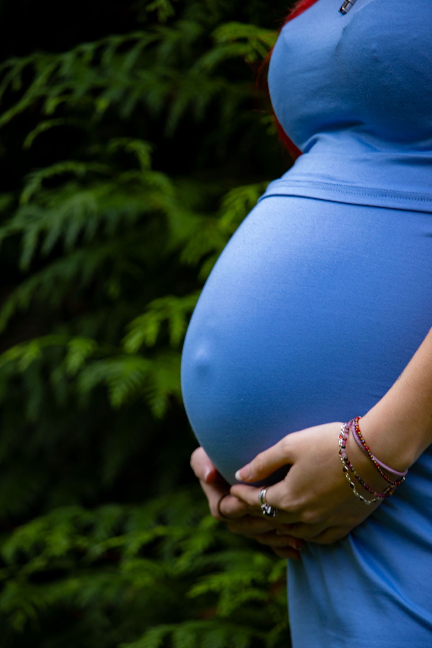 Close-up shots of pregnant belly against natural green foliage.