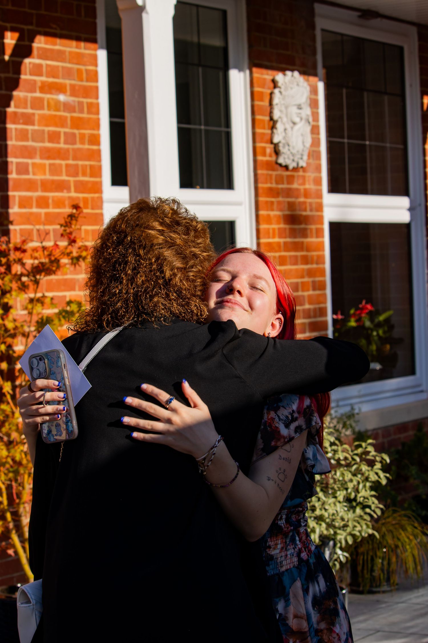 Two people sharing emotional embrace outside brick building in sunlight.