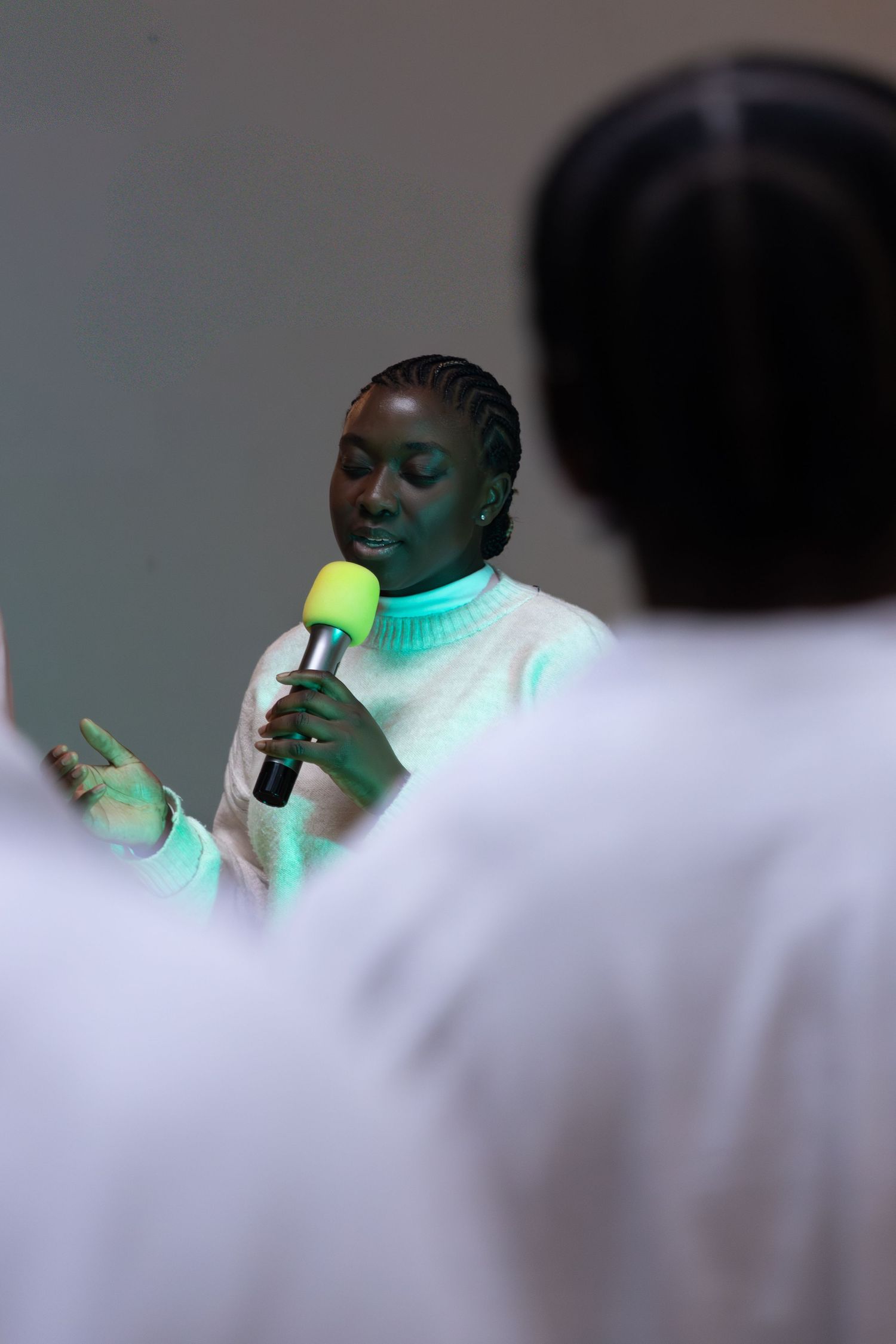 Worship member singing into a microphone during a church service, with congregation members in the foreground.
