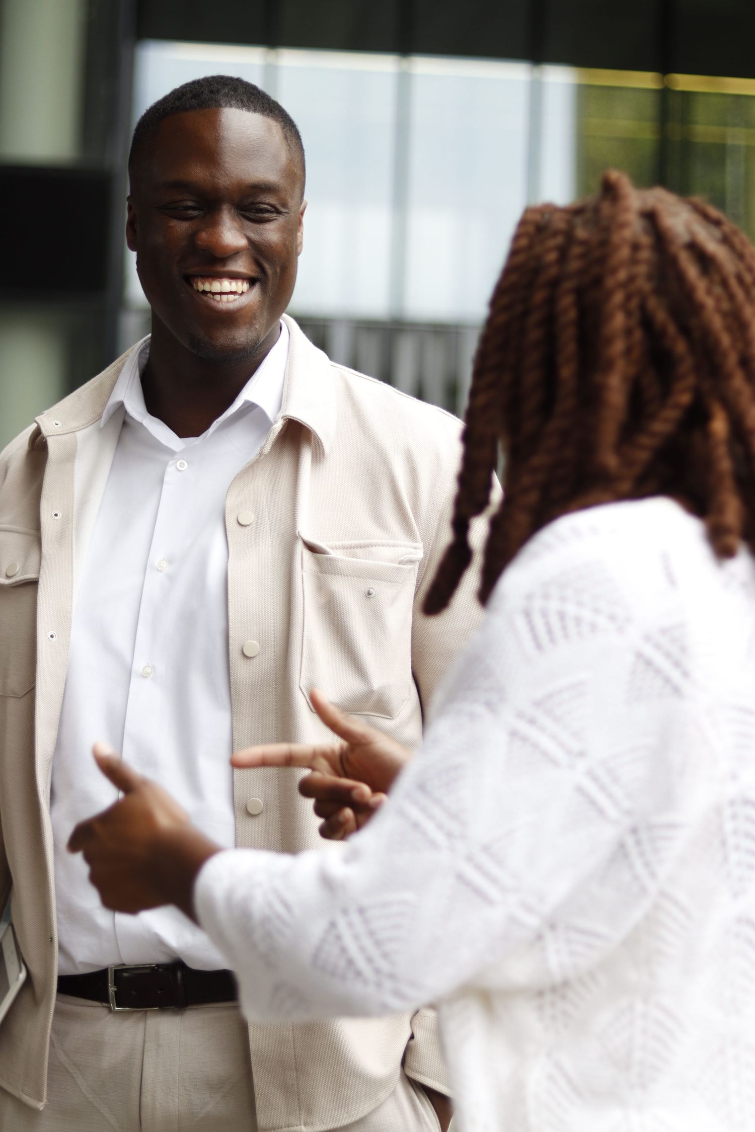 Candid moment of two people in light-toned outfits laughing and chatting outdoors, capturing a relaxed lifestyle interaction.