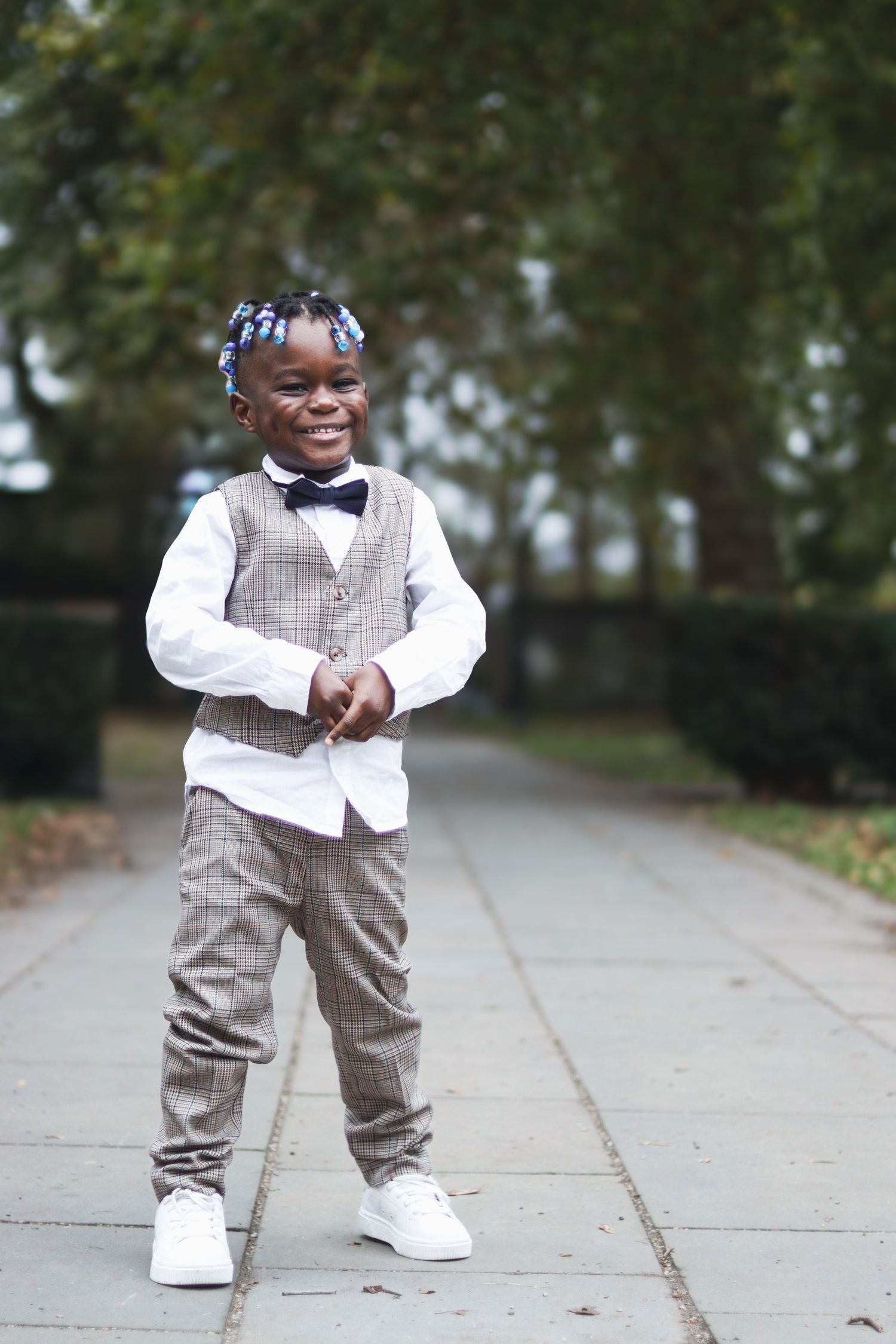 Young boy dressed in formal attire standing outdoors on a pathway during a wedding celebration.