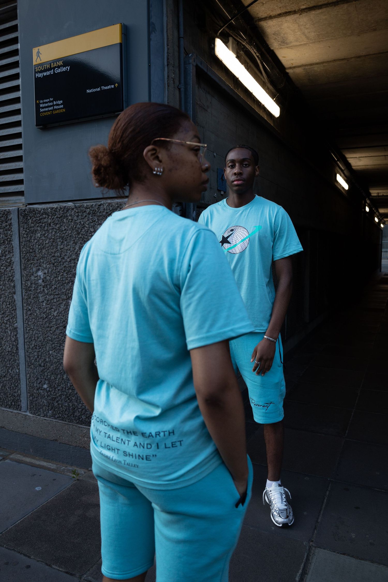 Models wearing coordinated light blue outfits pose through an urban alleyway during a streetwear clothing brand photoshoot.