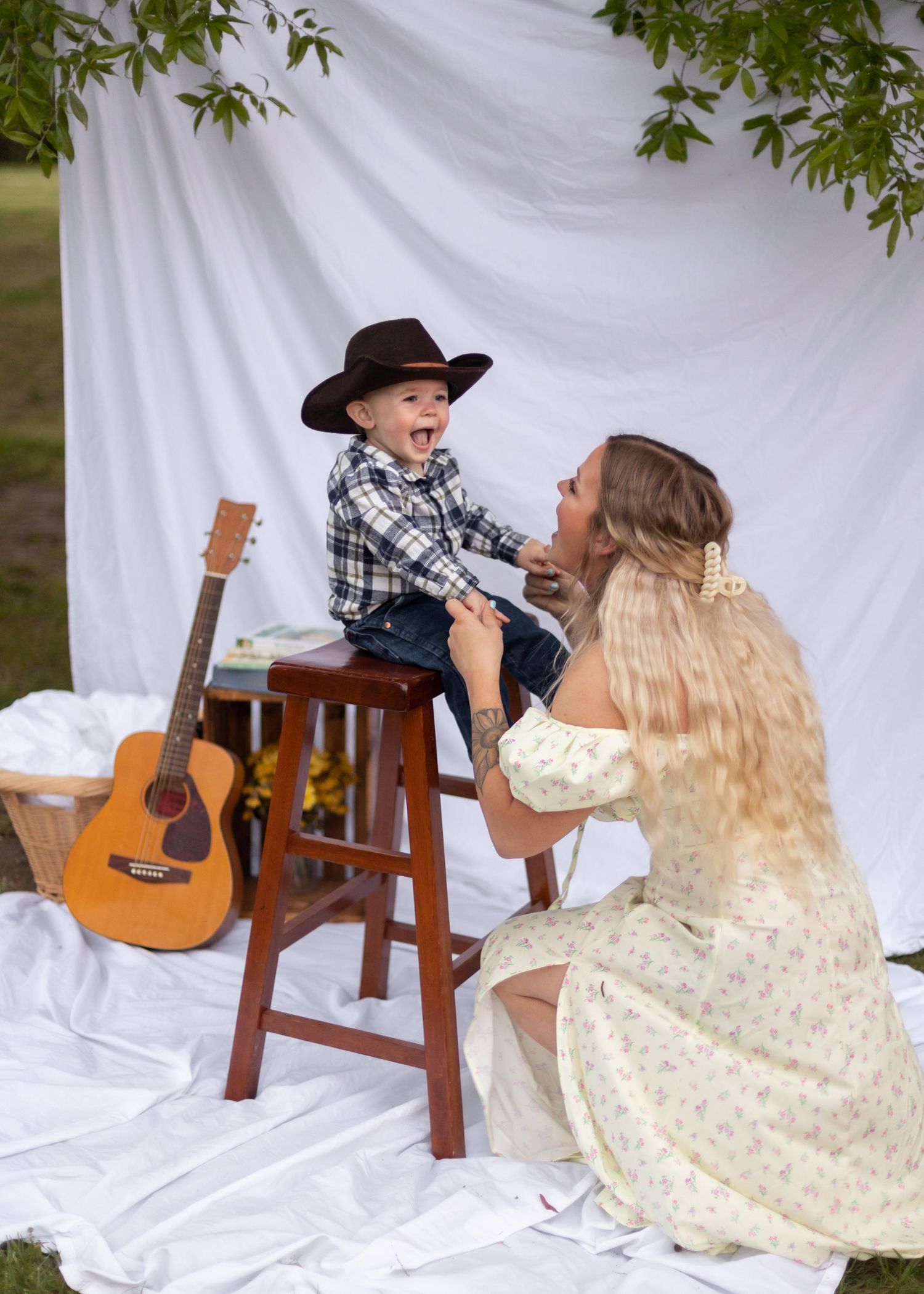 mom bending down to infant sitting on stool, hes smiling and wearing a cowboy hat