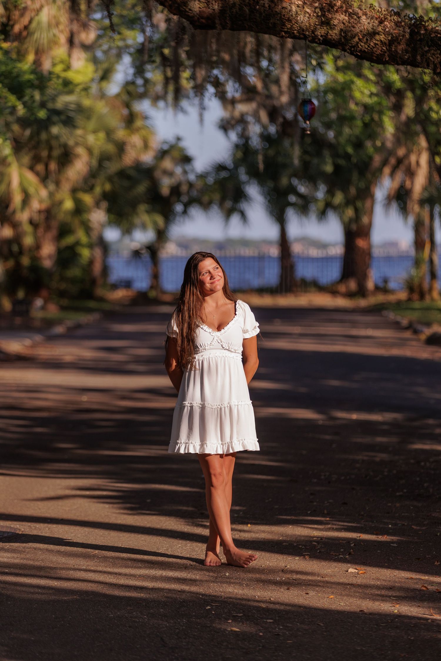 girl standing in sun, golden hour, trees, water in background