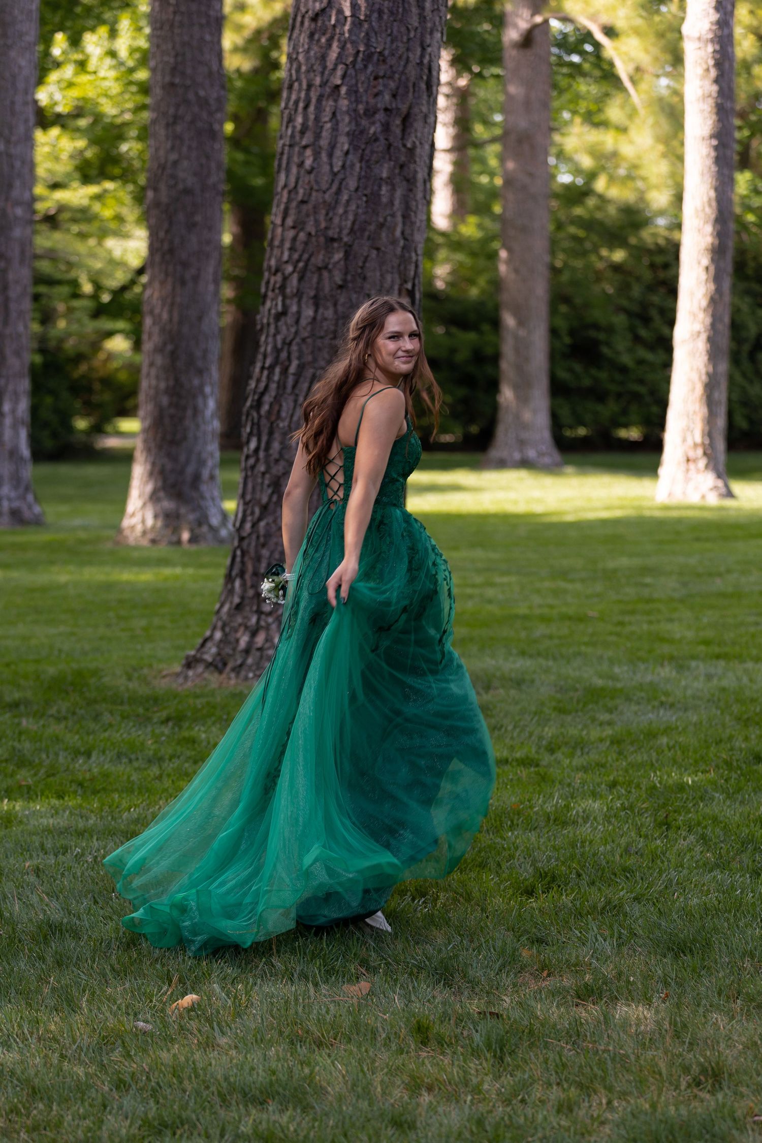 girl in ball gown prom dress, trees in background shes looking back at camera