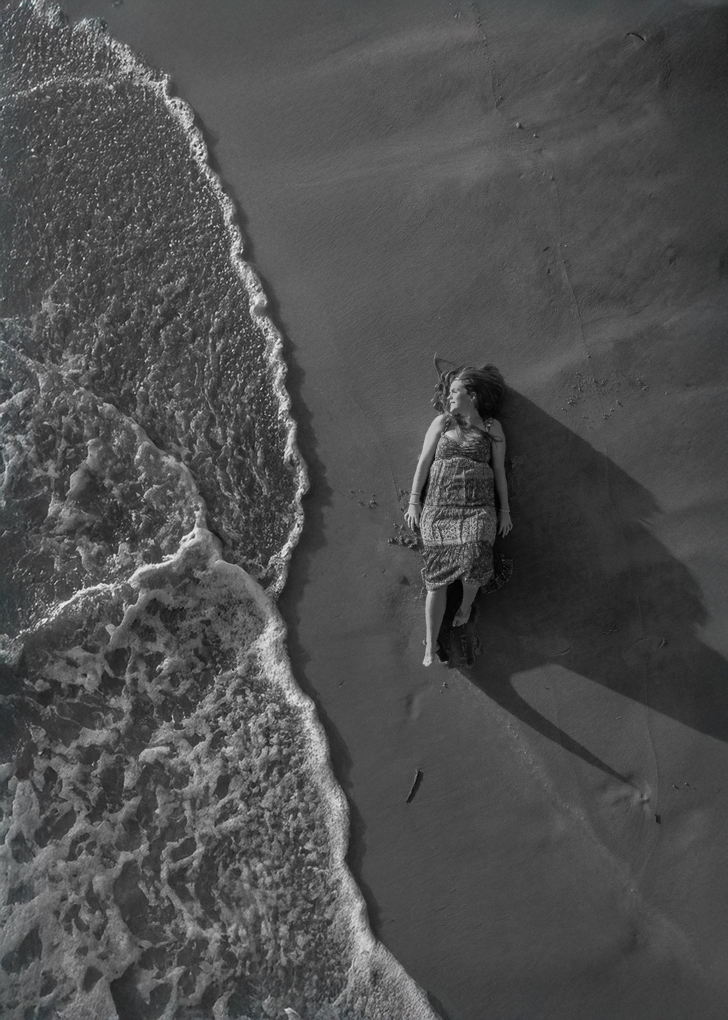 senior laying on beach next to water looking out, taken above with a drone