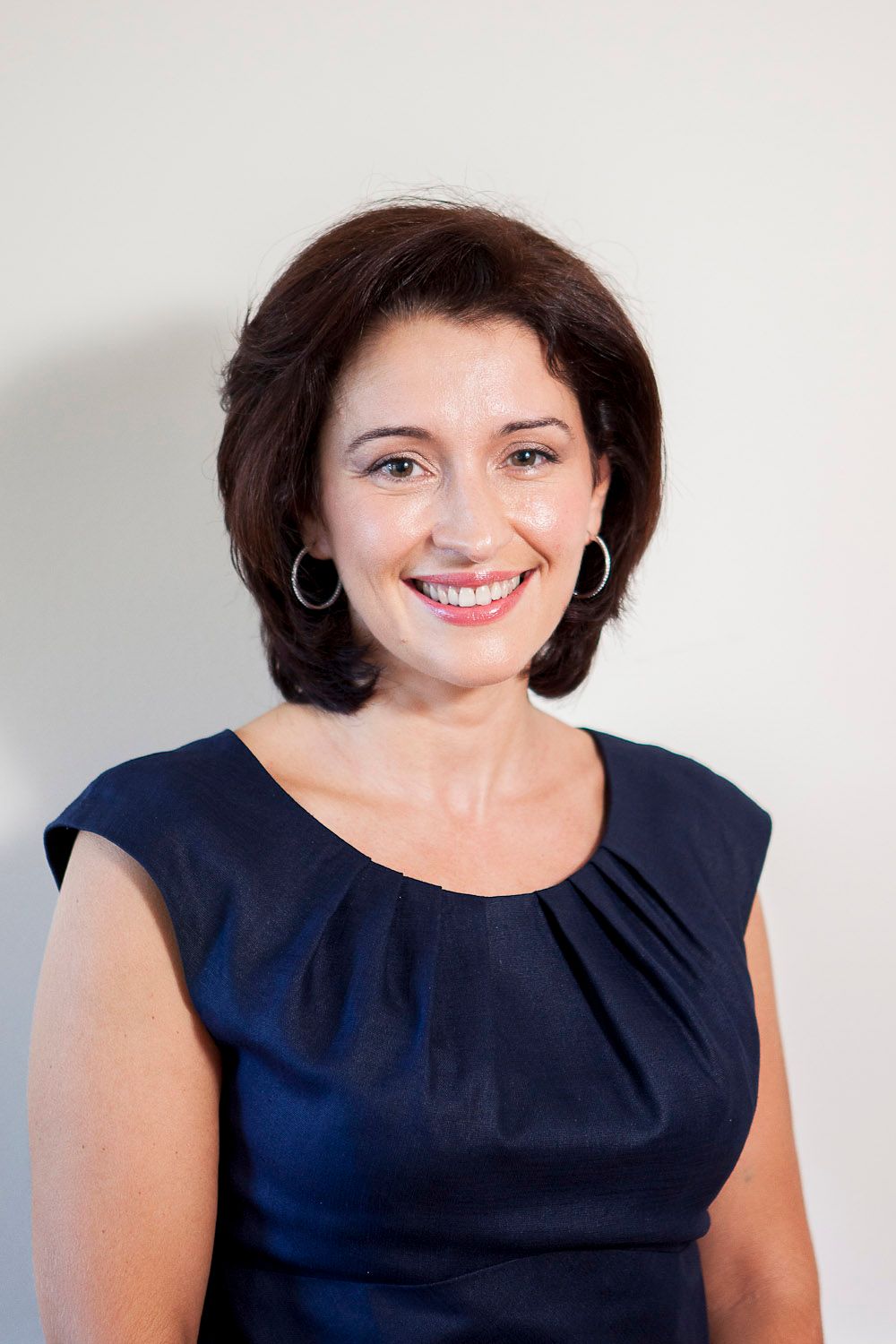 Smiling brunette woman in navy blue sleeveless dress posing for professional headshot.