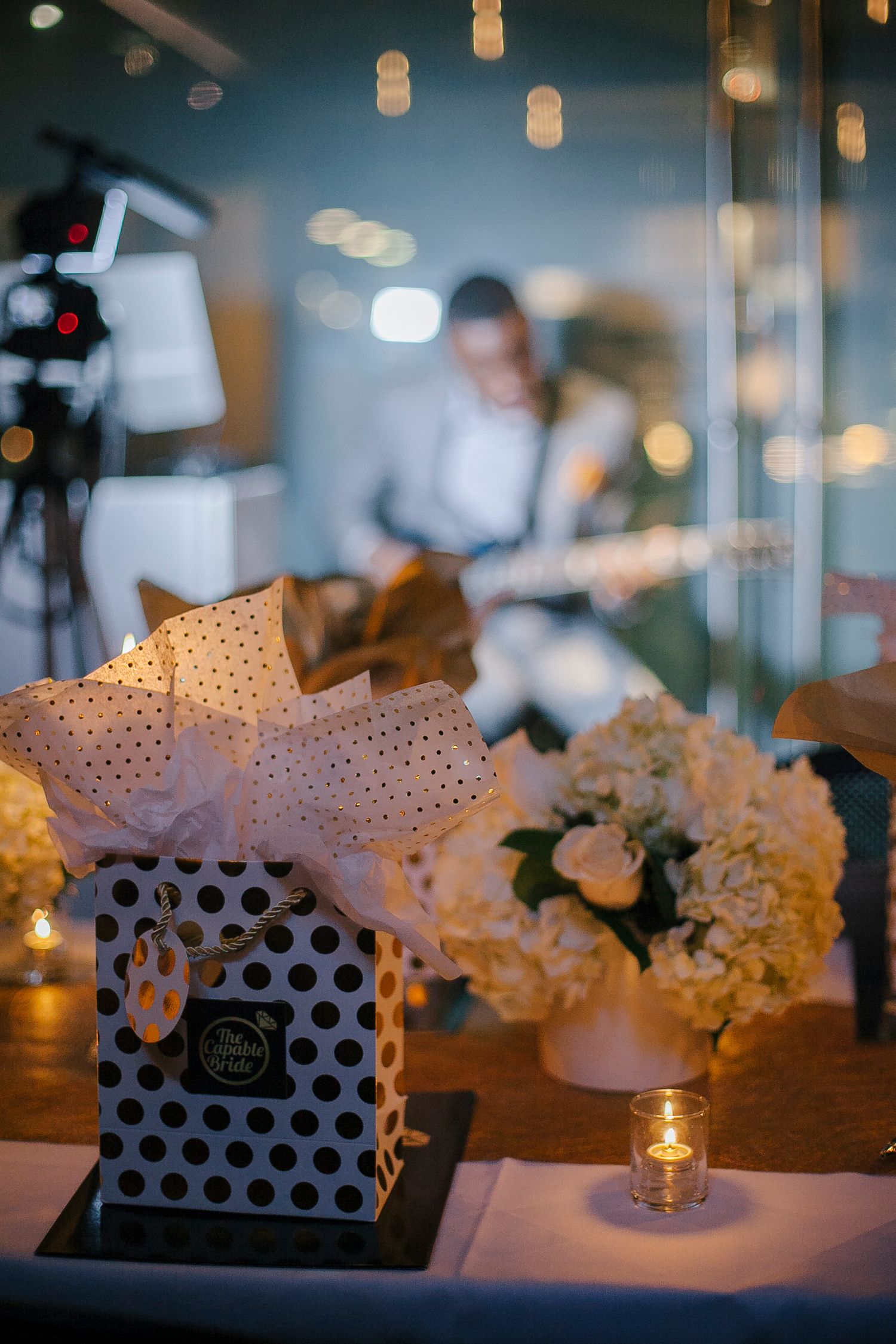 Elegant polka dot gift bag with white hydrangea floral arrangement at a candlelit wedding planning event.