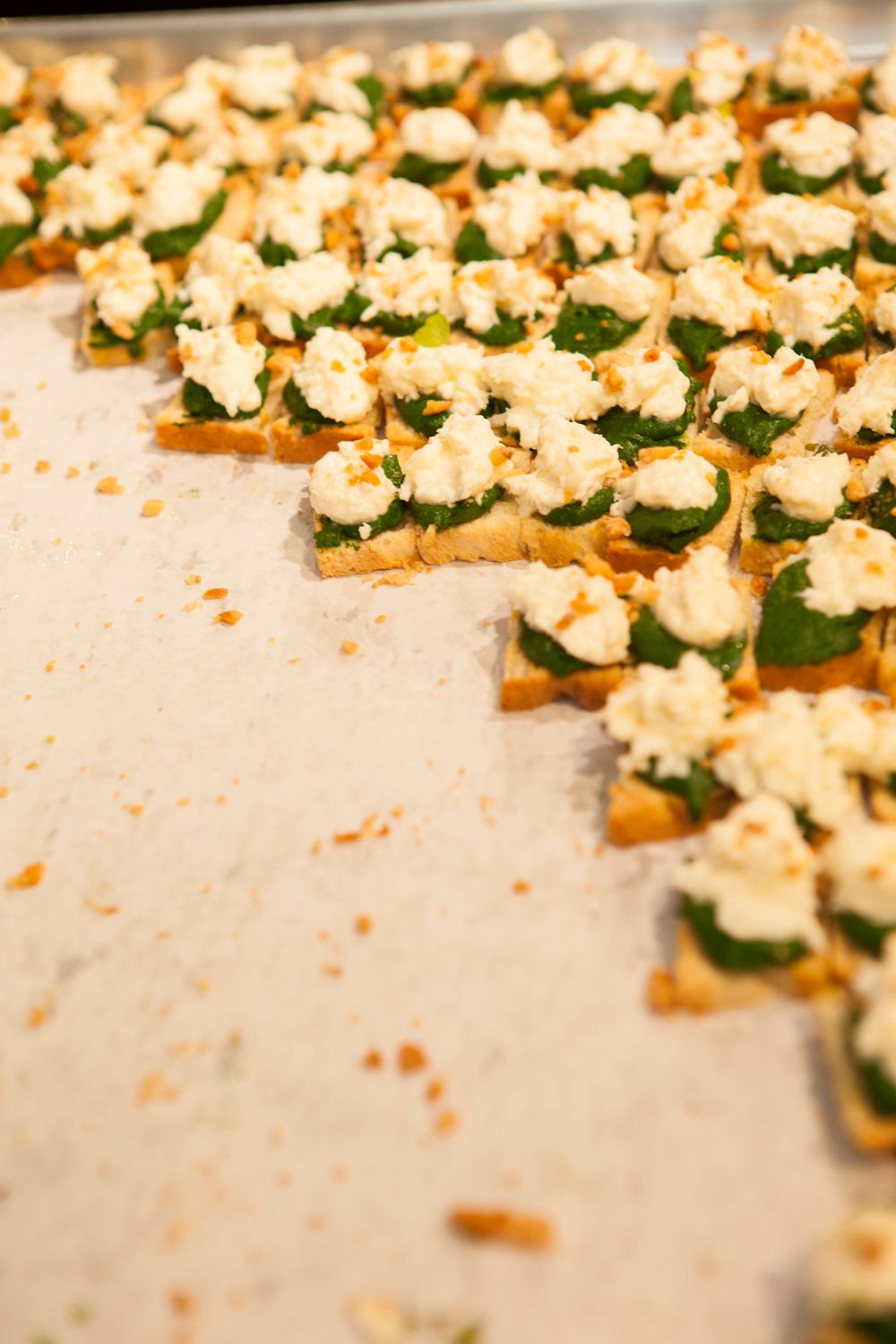 Rows of crostini topped with spinach and ricotta cheese arranged on a parchment-lined baking sheet.