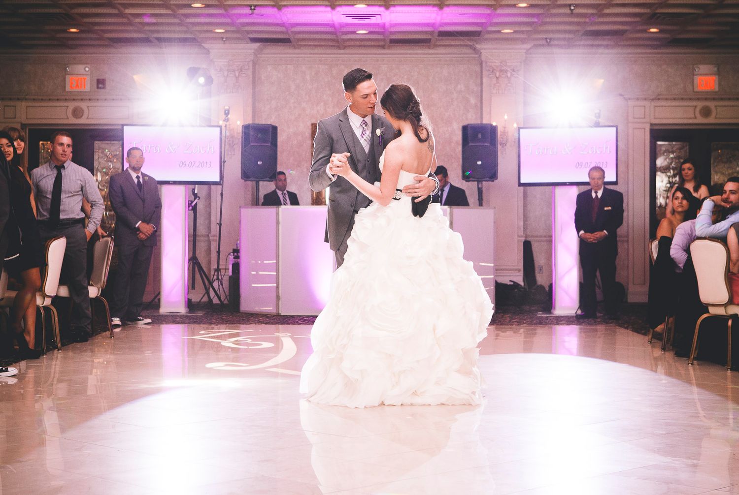 Bride and groom share their first dance on a white dance floor at a wedding reception.