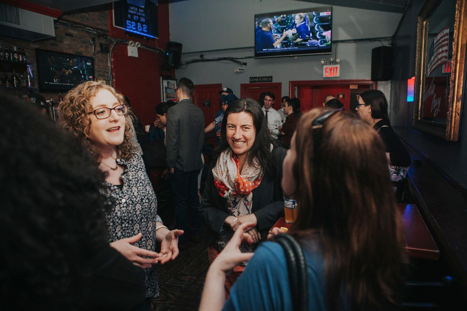 Women laugh and socialize at a crowded indoor bar networking event.