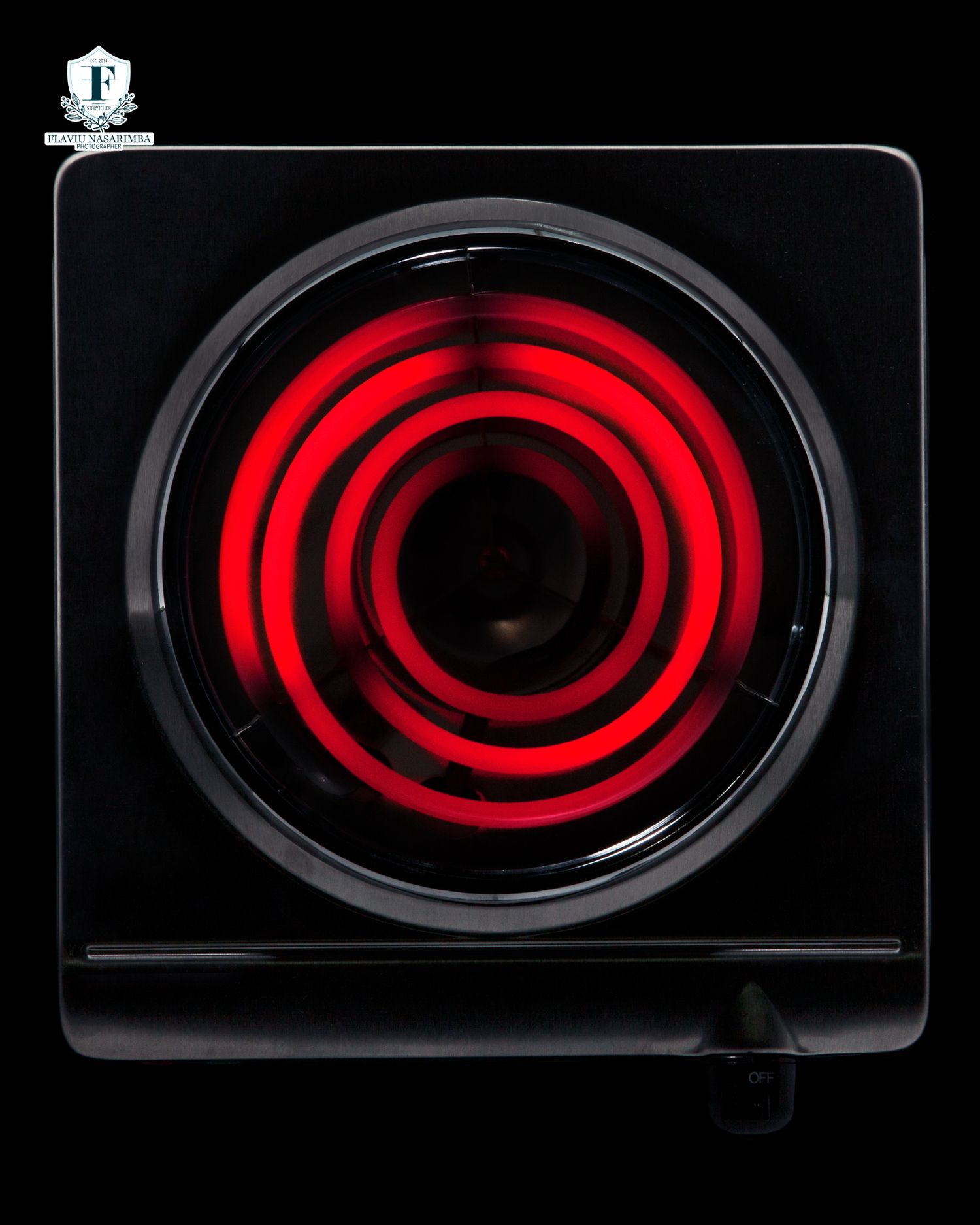 Glowing red electric coil burner on a black single hot plate cooker against dark background.
