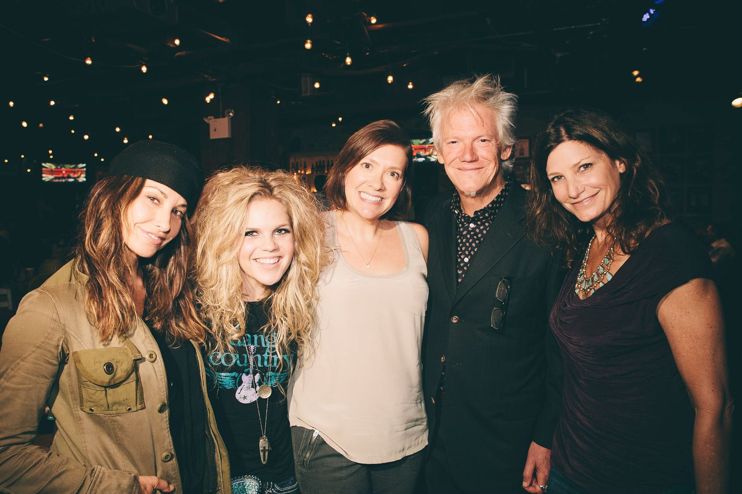 Five people smile together for a group photo at an indoor music venue event.