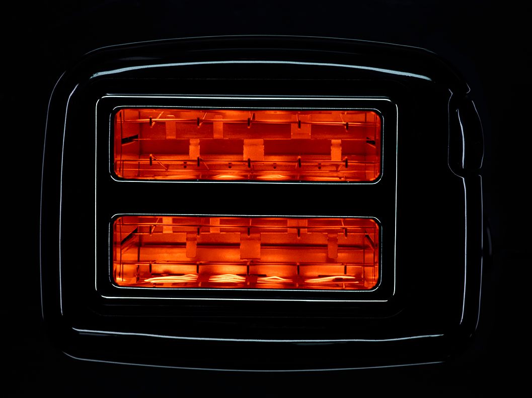 Close-up of a black toaster with glowing orange heating elements illuminated against a dark background.