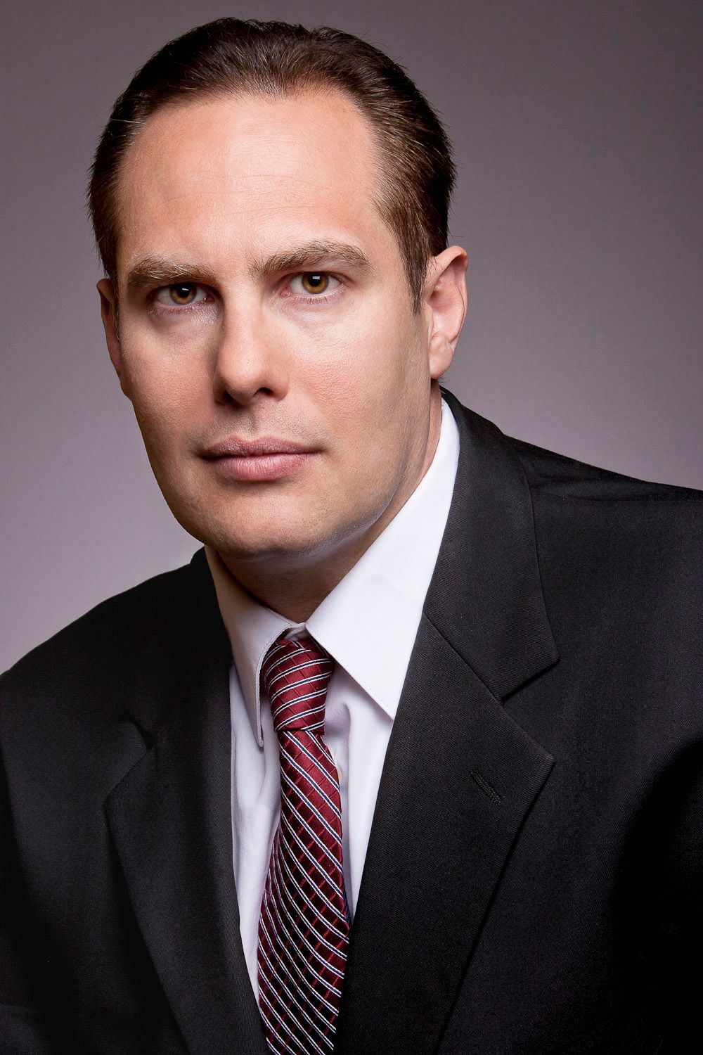 Professional businessman in black suit and striped tie posing for a corporate headshot.