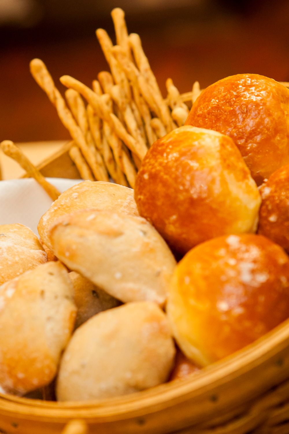 Assorted bread basket with golden dinner rolls, herb rolls, and crispy breadsticks in a woven basket.