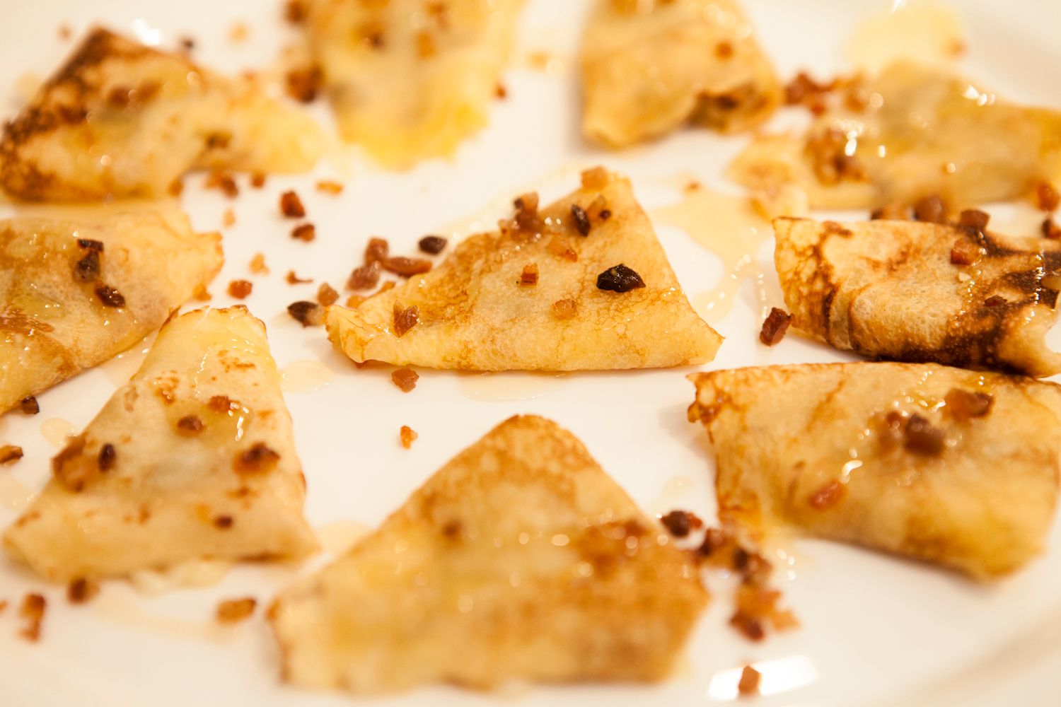 Golden fried wonton pieces topped with crunchy nuts and honey on a white plate.