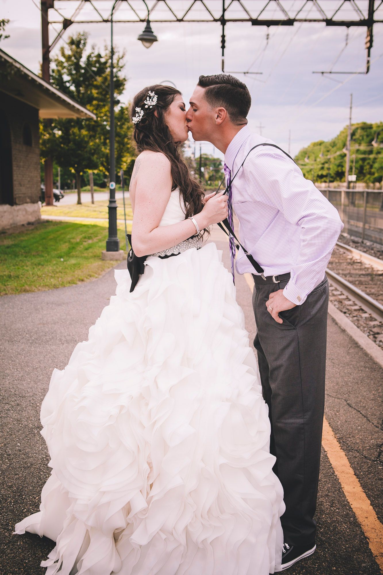 Bride and groom sharing a romantic kiss on a train station platform in their wedding attire.